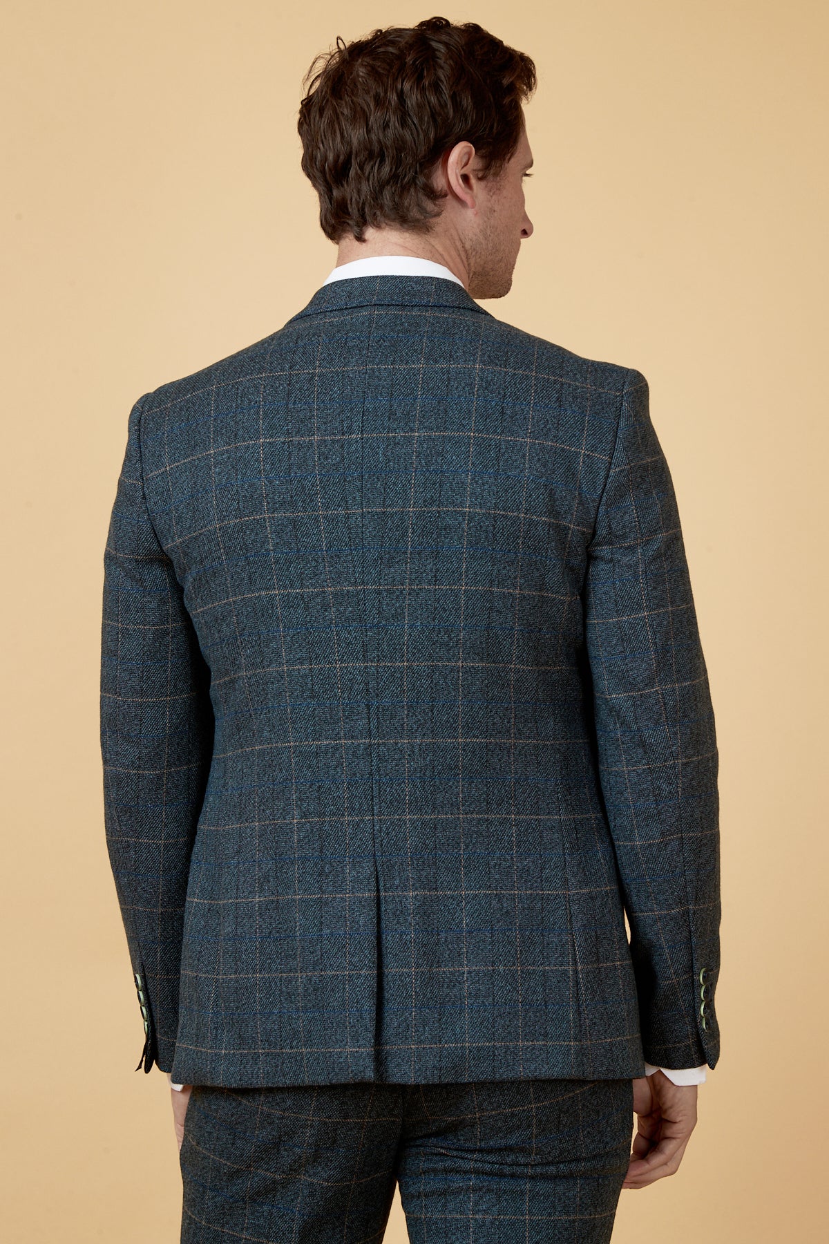 A man facing away from the camera wears the marcdarcy SCOTT Blue Tweed Check Blazer with matching trousers, featuring subtle navy velvet accents, set against a light beige background.