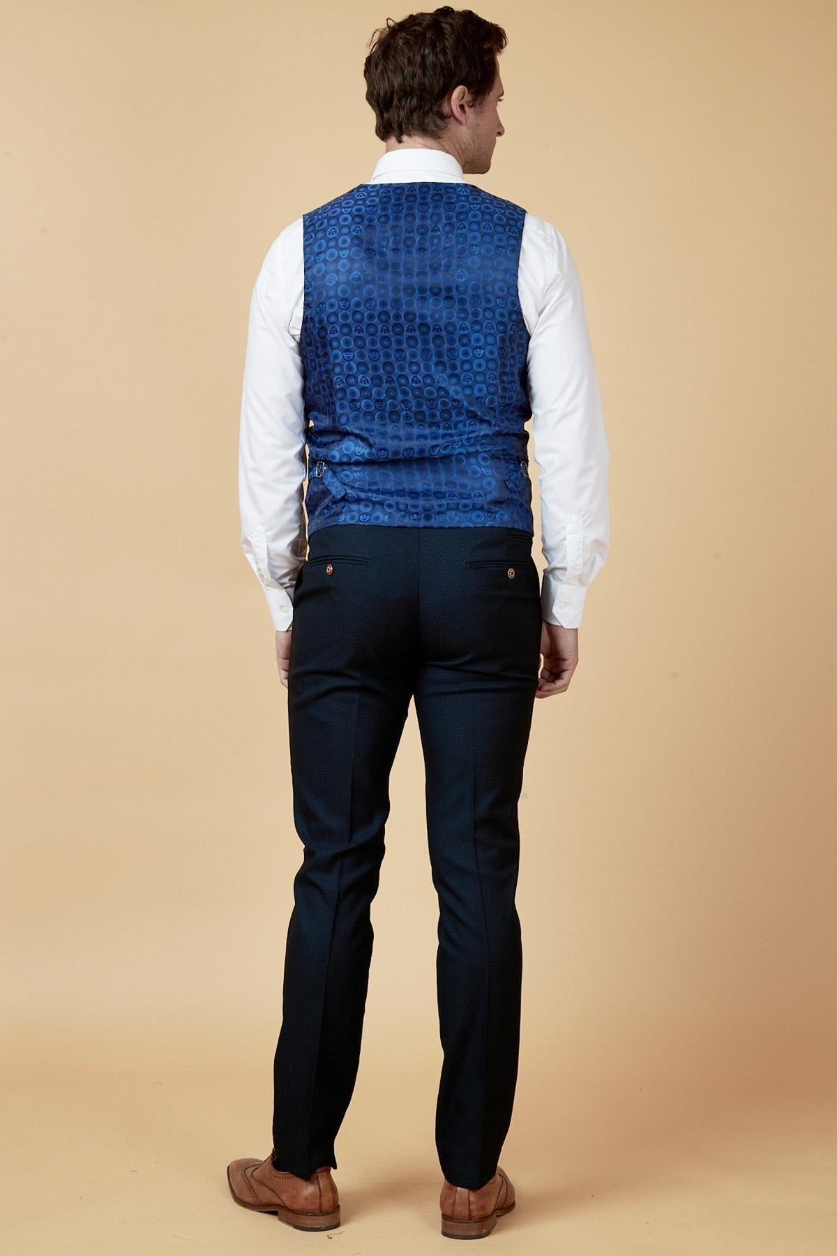 A man stands facing away against a beige background, wearing a white dress shirt, dark navy trousers, brown loafers, and the marcdarcy MAX - Navy Single Breasted Waistcoat—perfect for office wear.