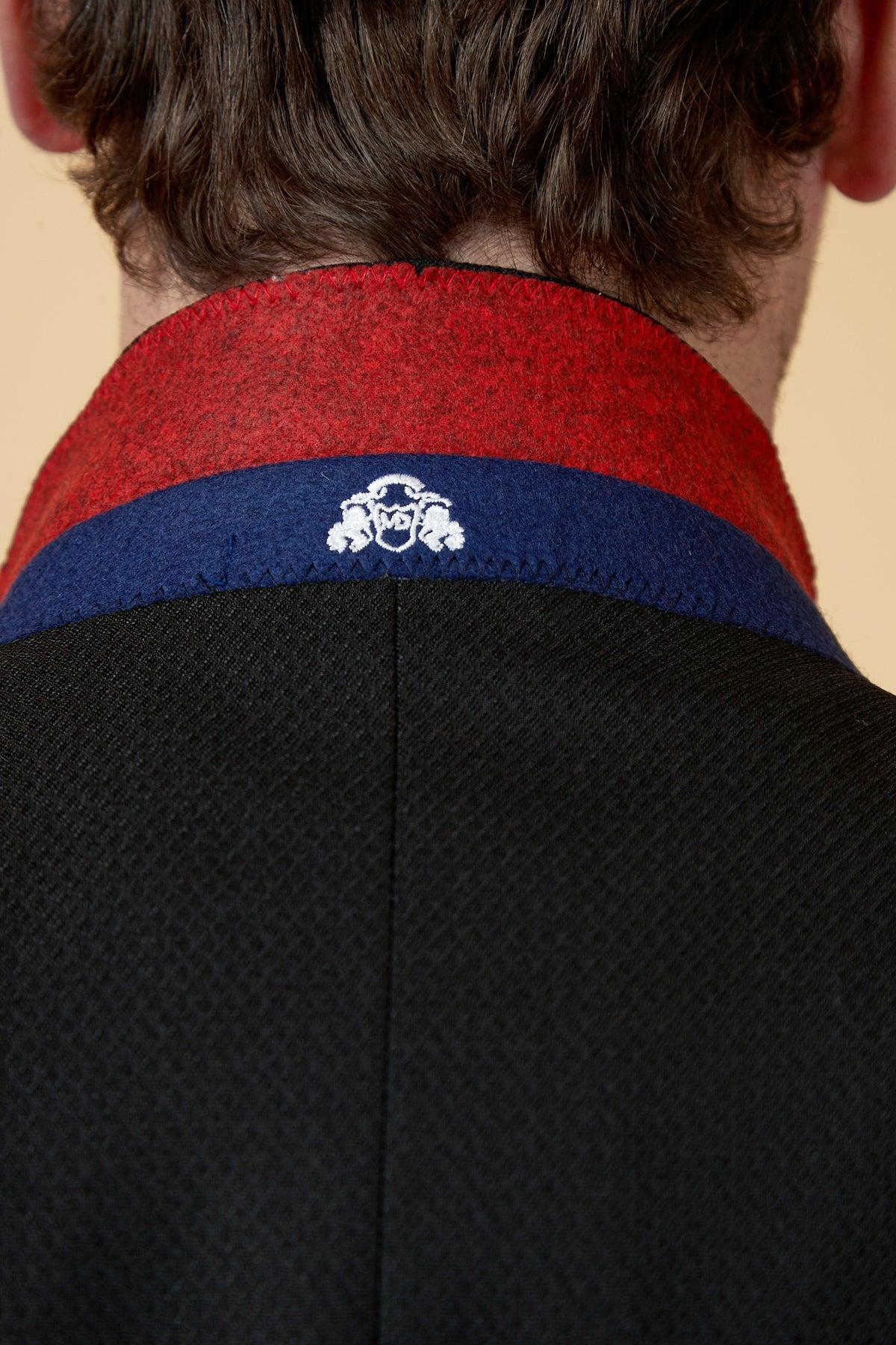 Close-up of the back of a person's neck and shoulders, featuring the marcdarcy MAX Black Three Piece Suit with contrast buttons, detailed with a red and blue collar and a small white embroidered crest at the center.