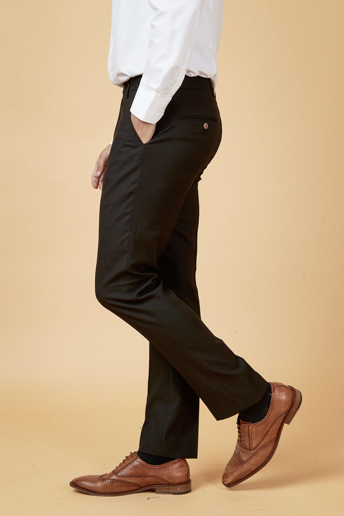 Man in a white dress shirt and marcdarcy MAX Black Trousers with Contrast Buttons, hand in pocket, showcasing classic workwear style with brown leather wingtip shoes.
