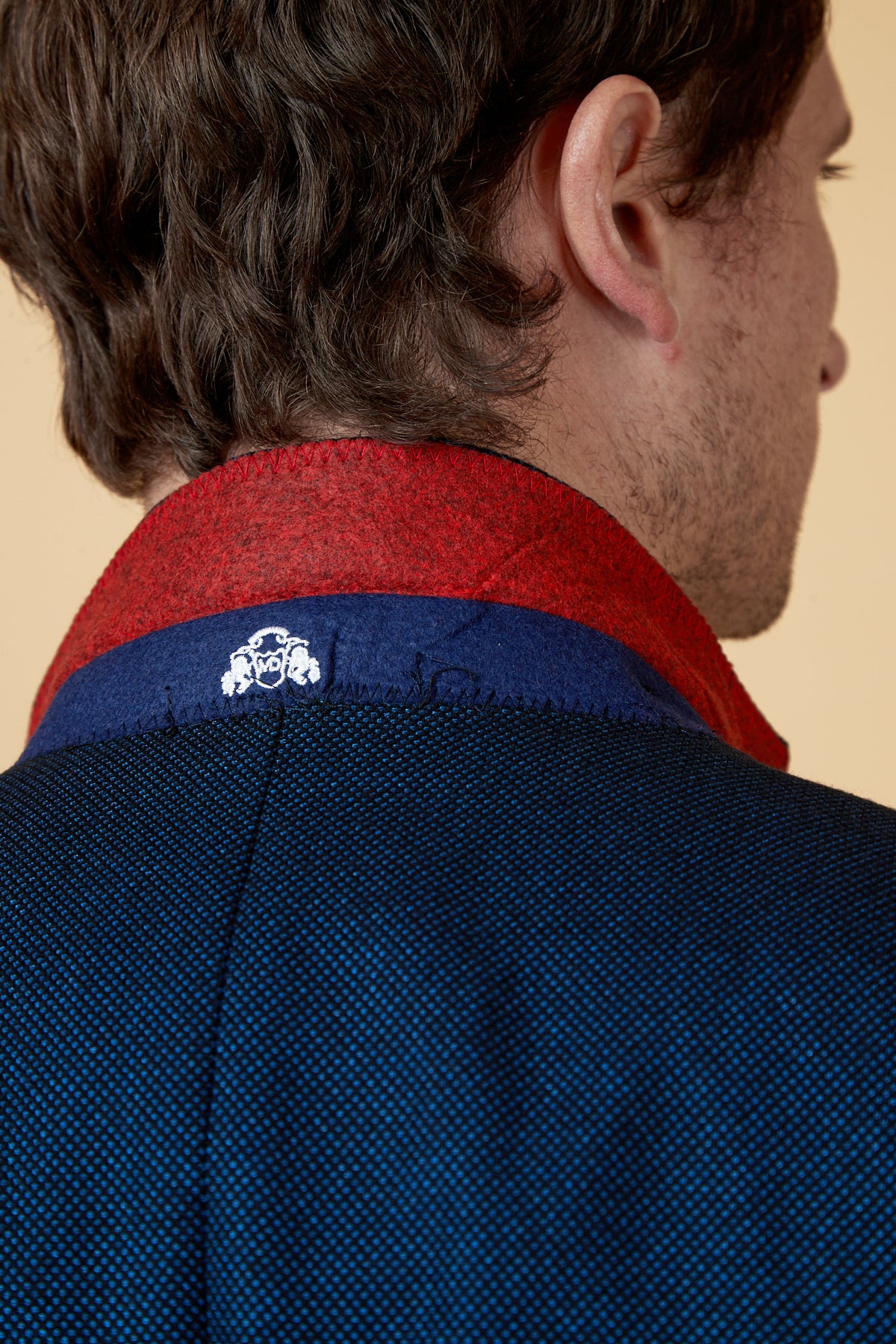 Close-up of the back of a man's head and shoulder wearing the marcdarcy CALLUM Blue Three Piece Suit, featuring a textured blue slim fit jacket with a red and navy collar and white logo—perfect for grooms or formal events.
