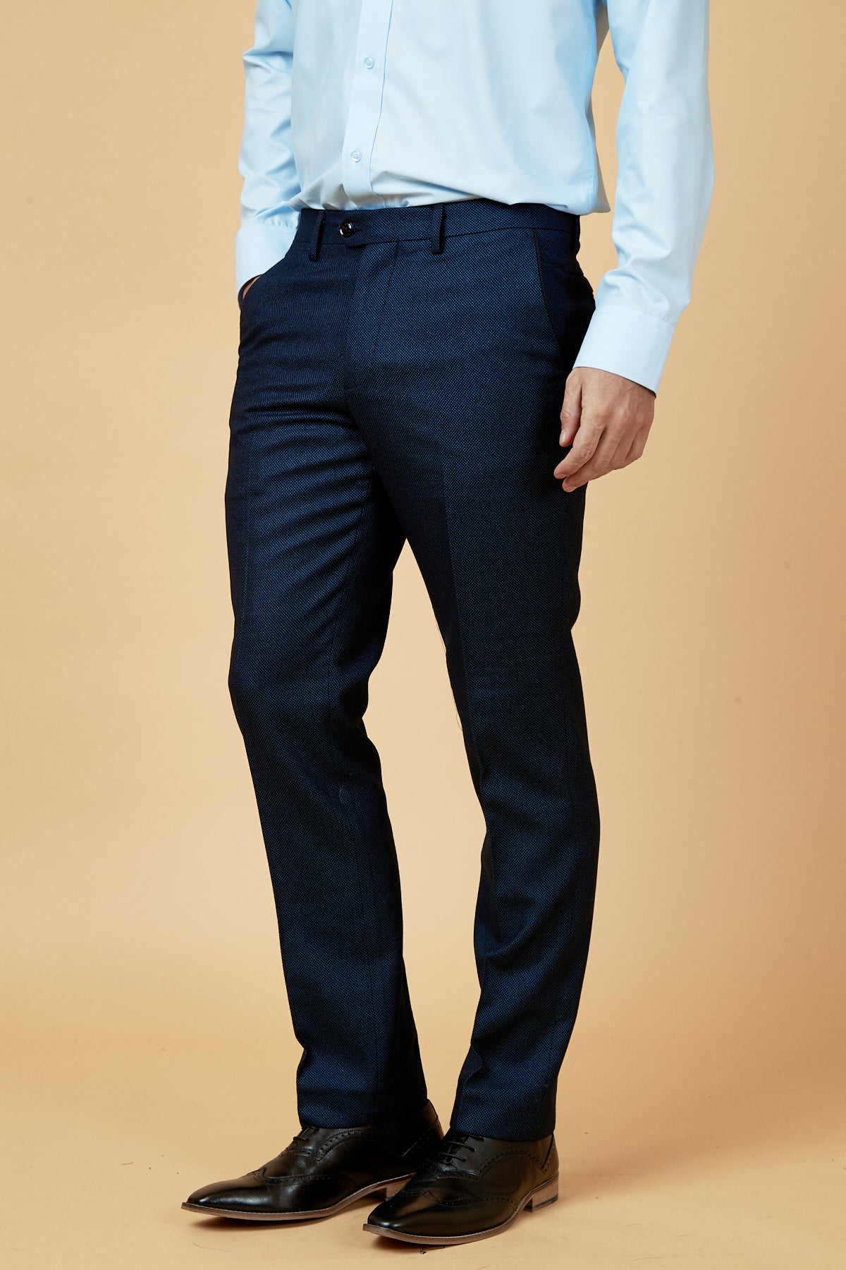 A man models the marcdarcy CALLUM Blue Three Piece Suit, standing with hands in pockets against a beige background for a polished formal look. His head is not visible in the image.