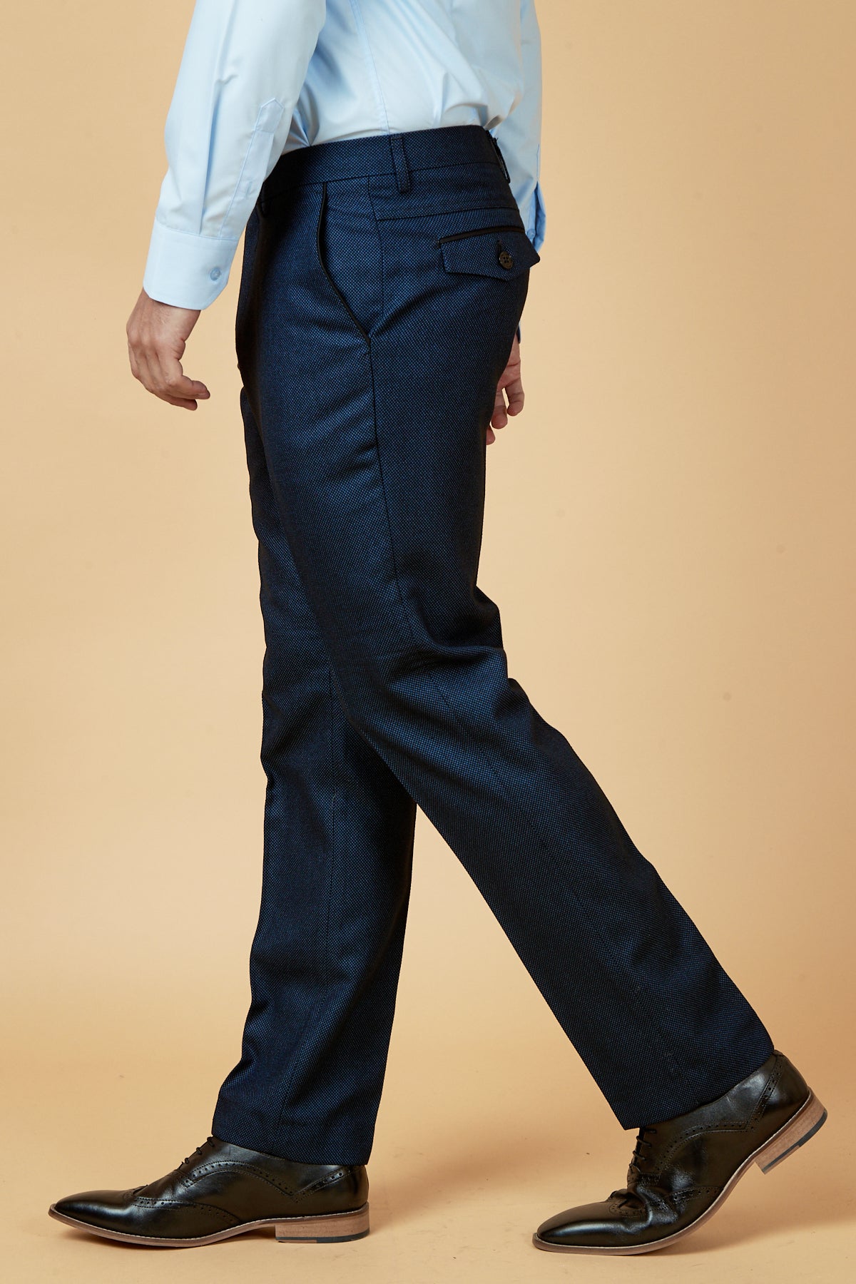 A person in the CALLUM Blue Three Piece Suit by marcdarcy is walking, shown in profile against a beige background.
