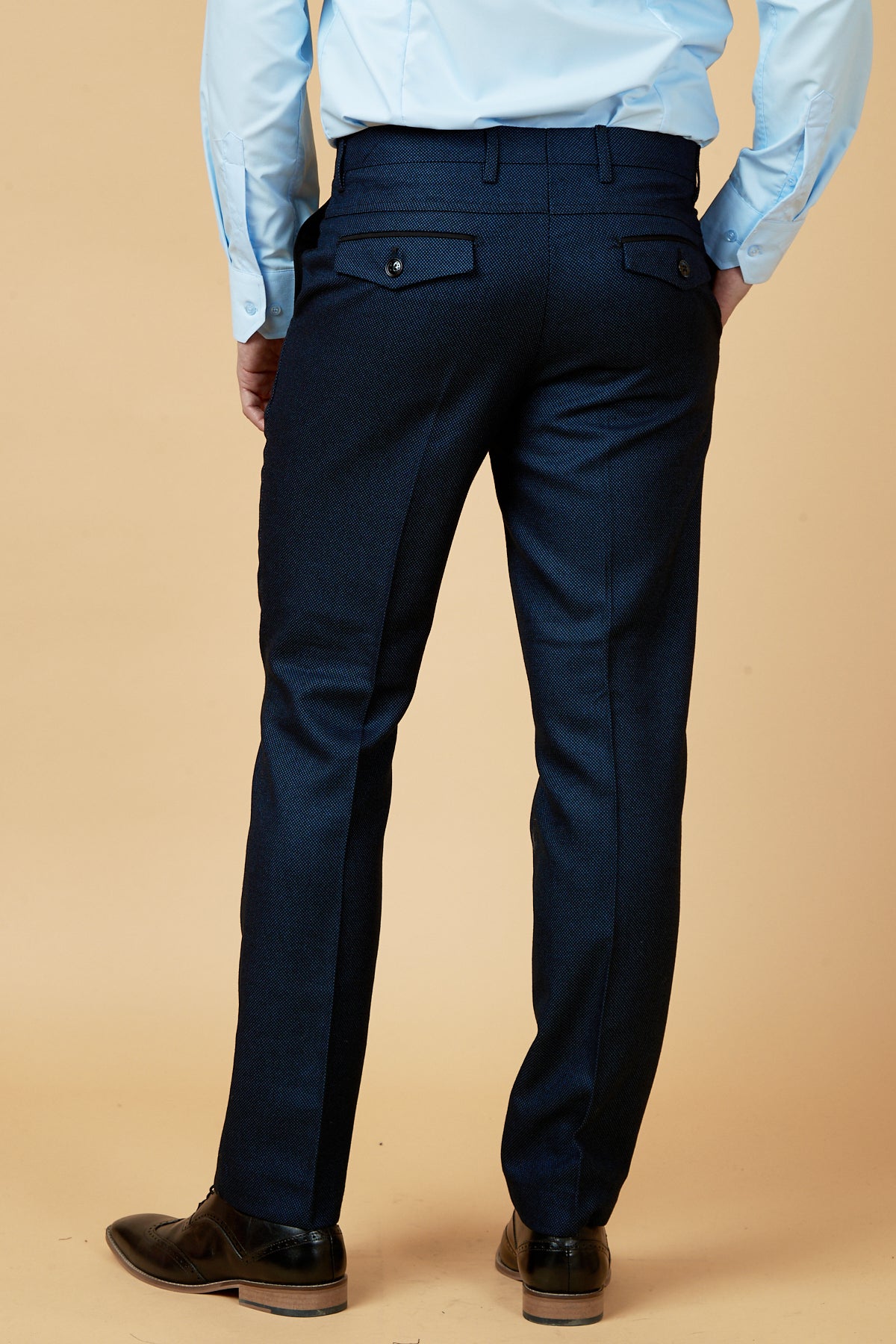 Dressed in the marcdarcy CALLUM - Blue Three Piece Suit, a person stands with their back to the camera against a beige background, highlighting a polished formal look.