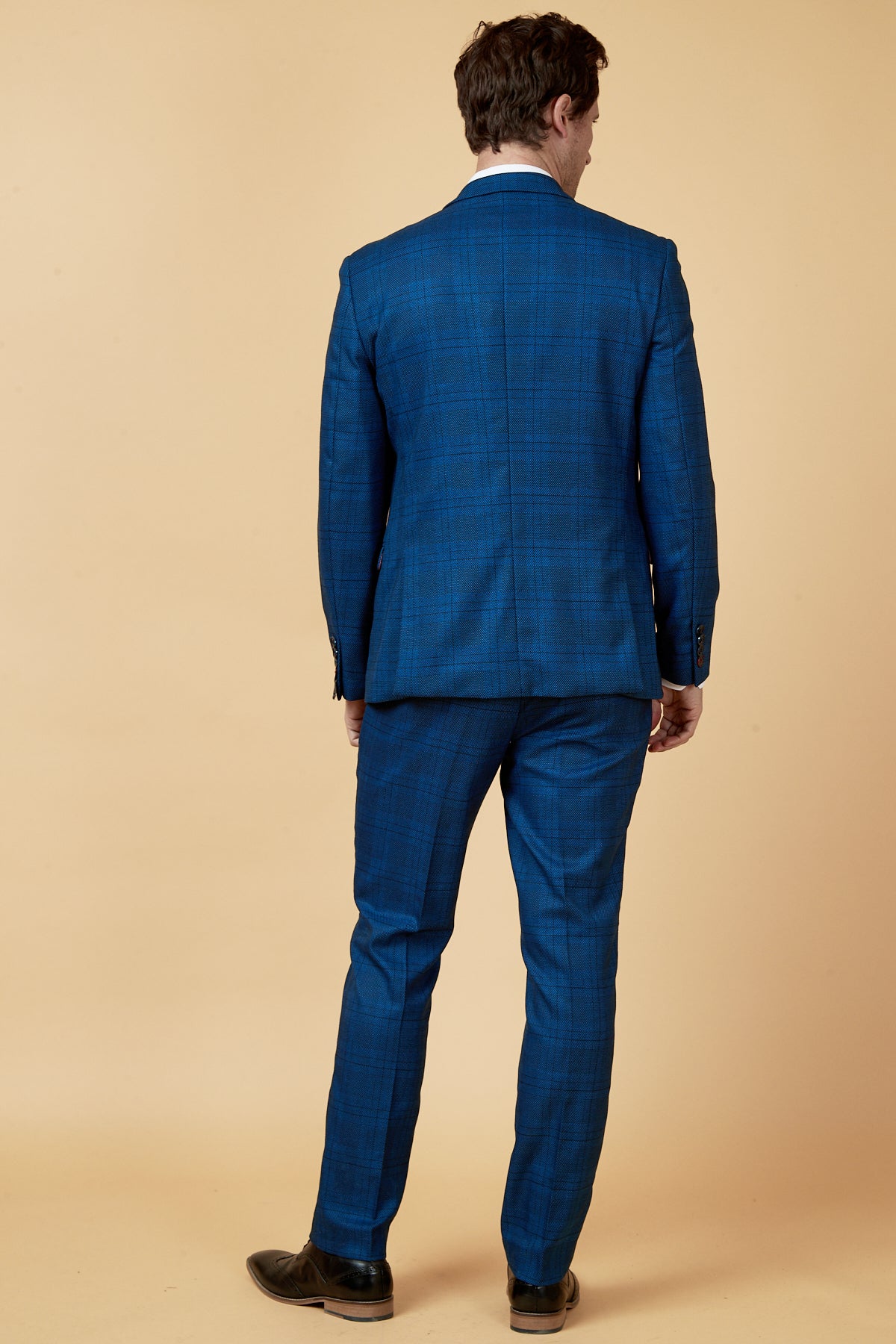 A man faces away, wearing the marcdarcy JERRY - Blue Check Blazer and black dress shoes, set against a plain beige background.