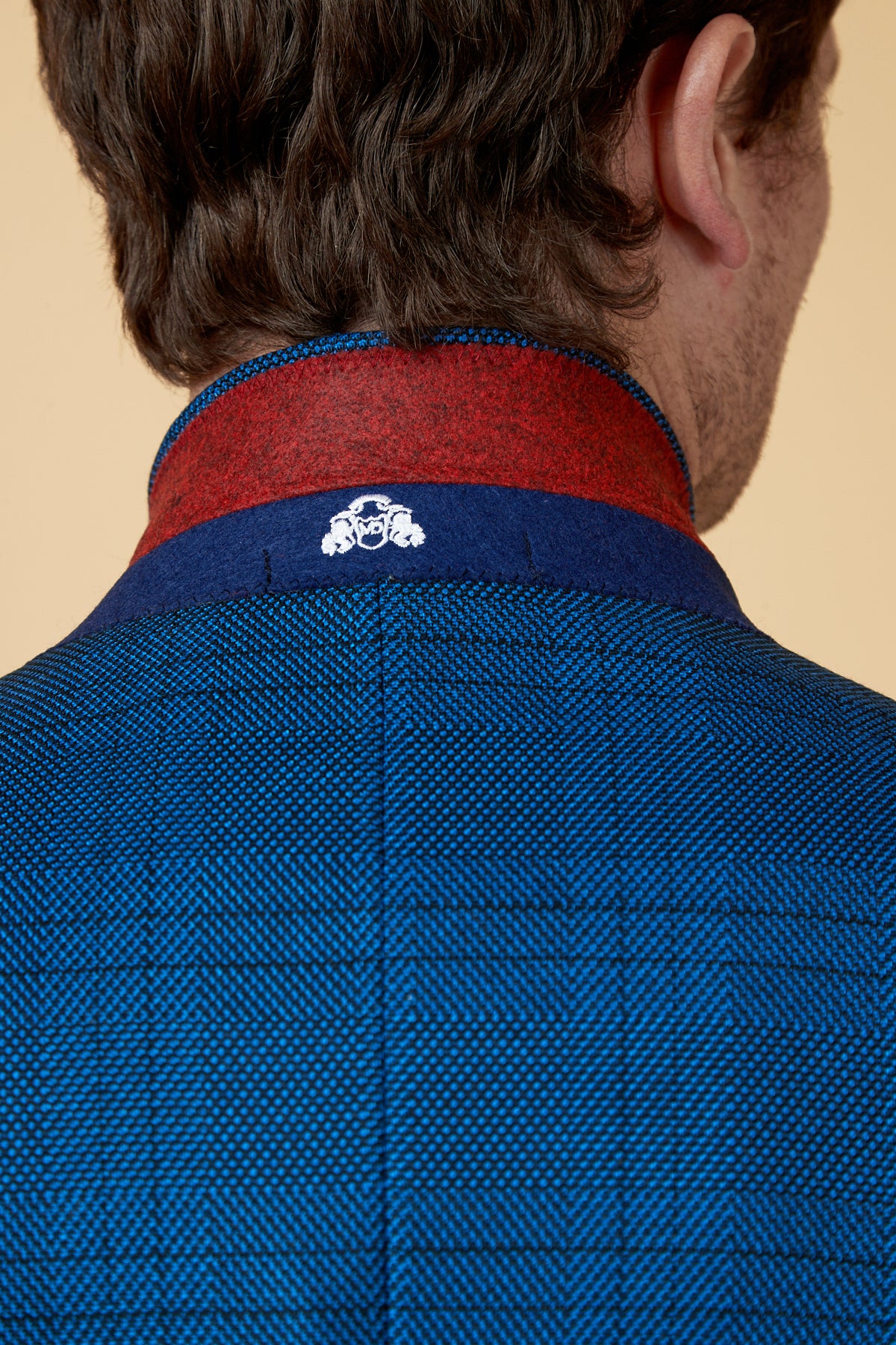 A close-up of a mans neck and shoulders wearing the marcdarcy JERRY Blue Check Blazer, highlighted by its textured finish and red and navy collar with a small white face-and-hands logo on the slim fit collar.