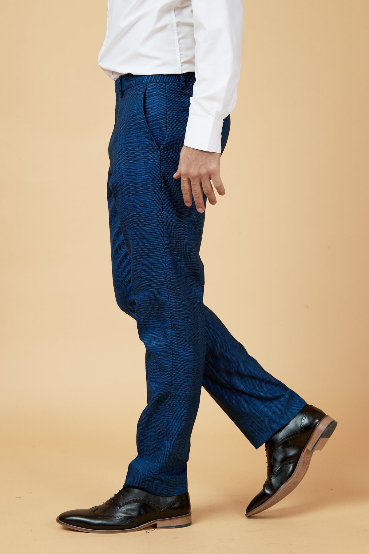 A person models marcdarcy's JERRY - Blue Check Trousers with a white shirt and black dress shoes, standing against a beige background in a side profile view (neck down).