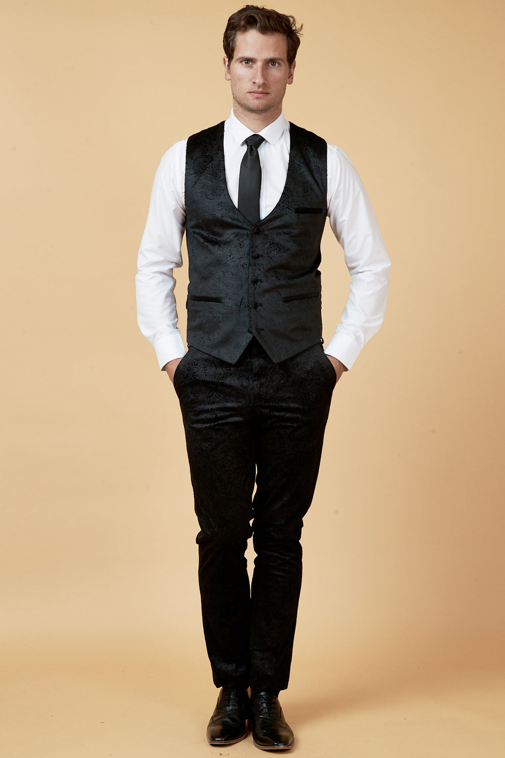 Man in a marcdarcy SIMON Black Velvet Jacquard Waistcoat with matching pants, white dress shirt, black tie, and black dress shoes.