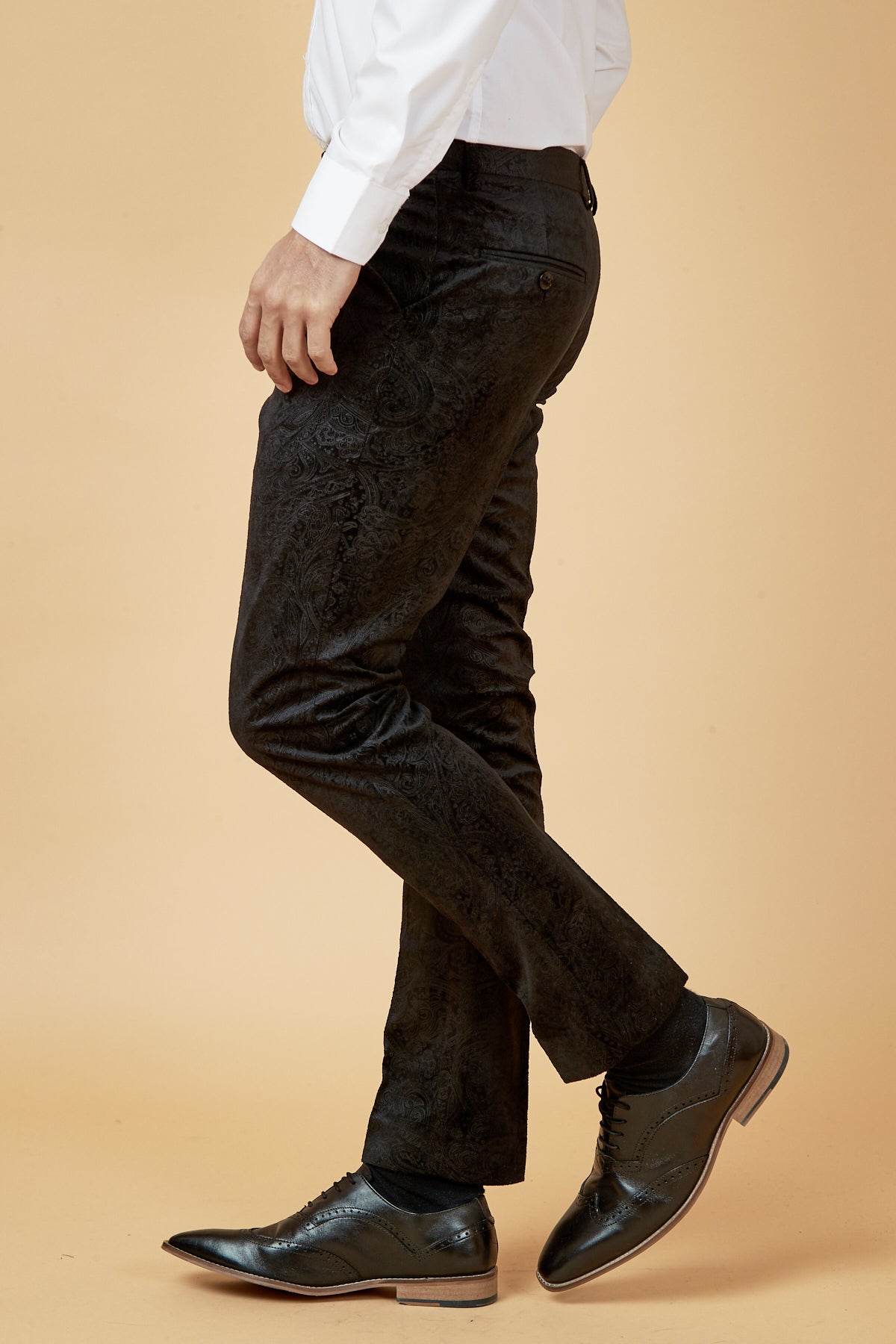 A person wearing a white dress shirt, Marc Darcy SIMON Black Velvet Jacquard Trousers, and black dress shoes stands against a beige background, shown from the shoulders down and facing left.