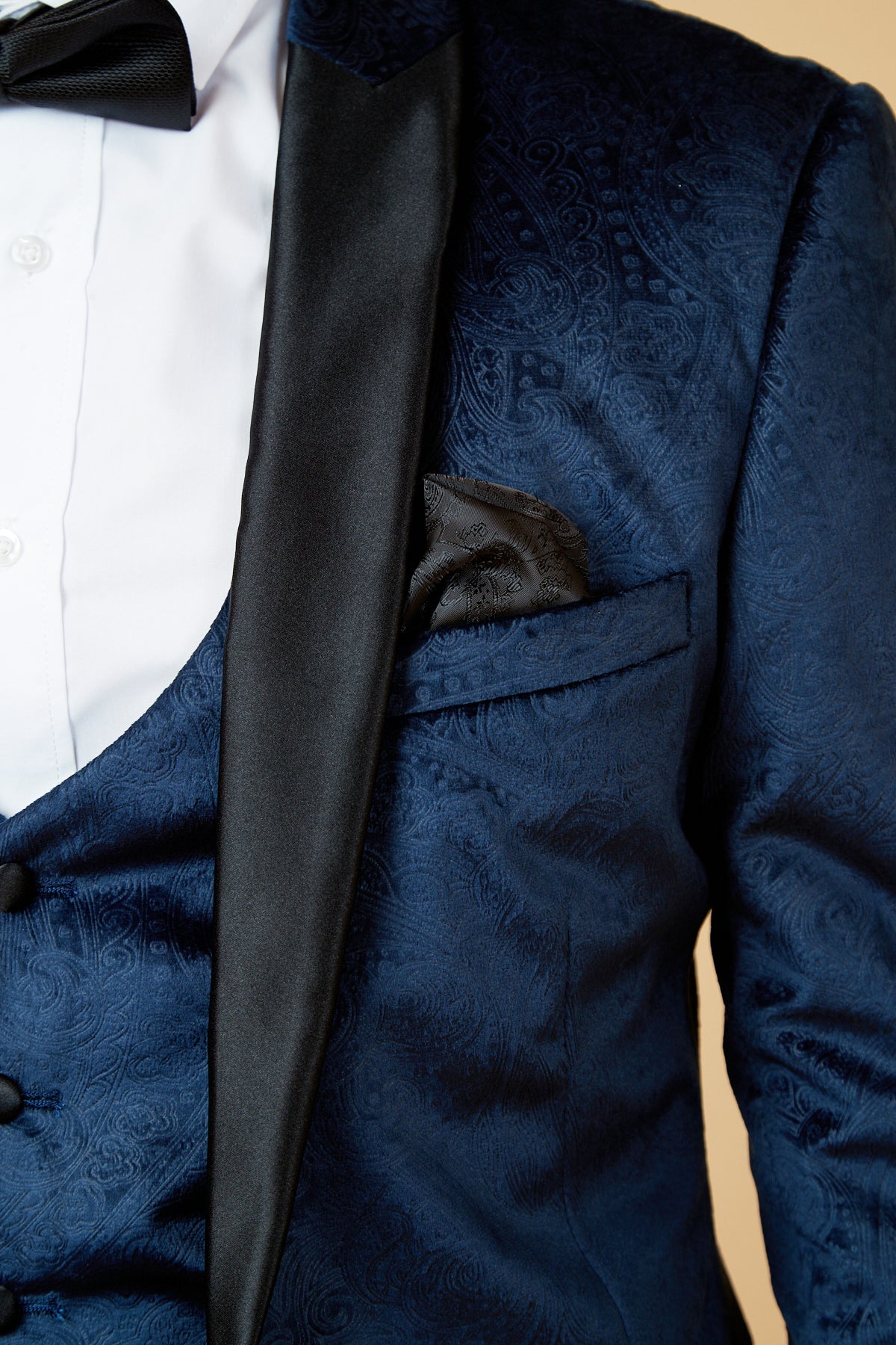 Close-up of a man wearing the Marc Darcy SIMON Navy Velvet Jacquard Three Piece Suit, showcasing its paisley-patterned jacket with black satin lapel, white shirt, black bow tie, and pocket square. Focus is on the upper torso.