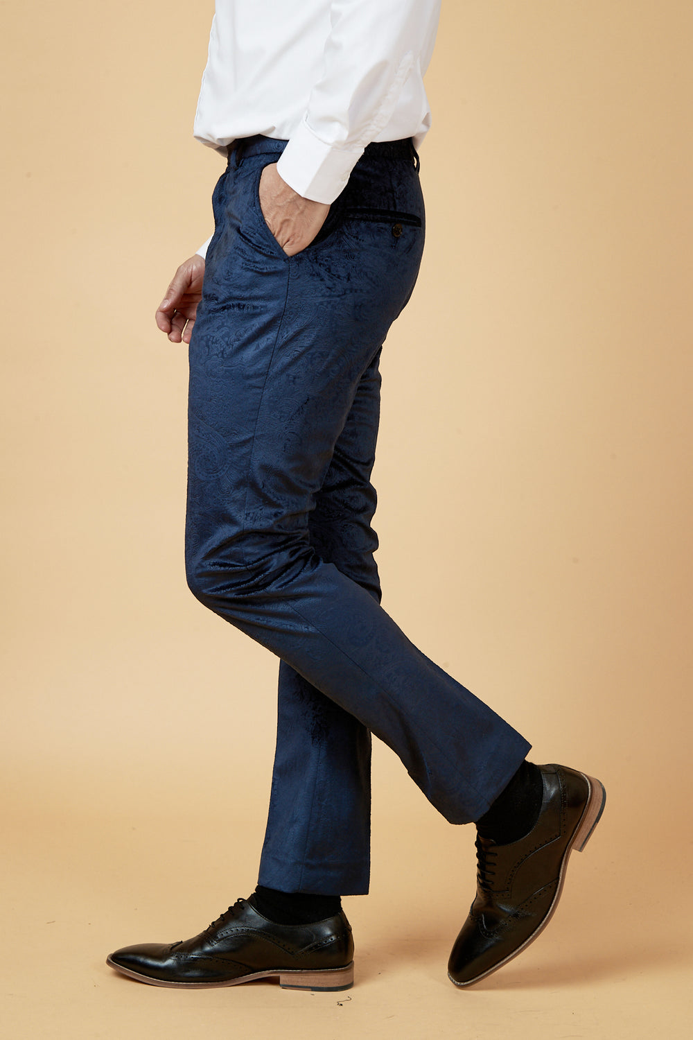 A man, shown from the shoulders down in profile against a plain beige background, wears a white dress shirt, black dress shoes, and Marc Darcy SIMON - Navy Velvet Jacquard Trousers.