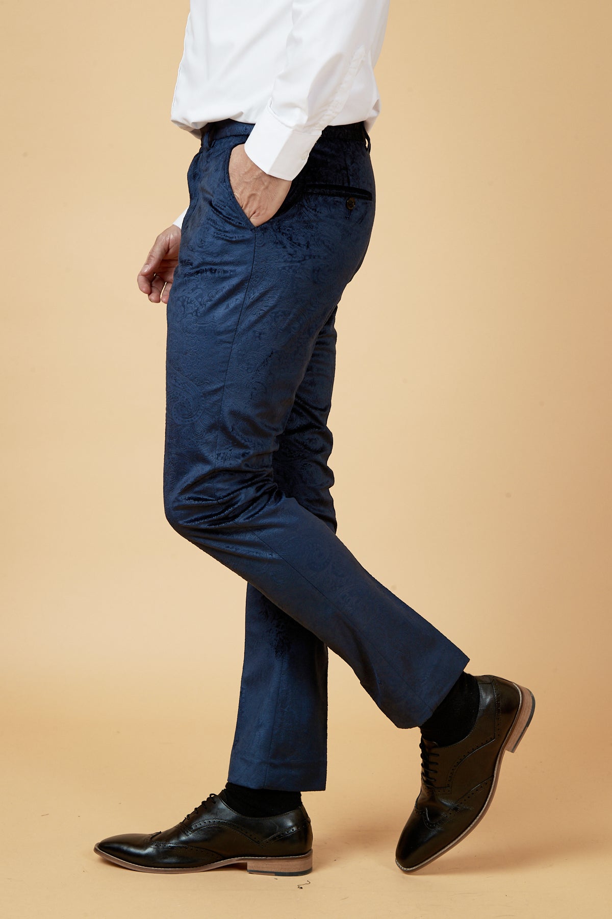 A man, shown from the shoulders down in profile against a plain beige background, wears a white dress shirt, black dress shoes, and Marc Darcy SIMON - Navy Velvet Jacquard Trousers.
