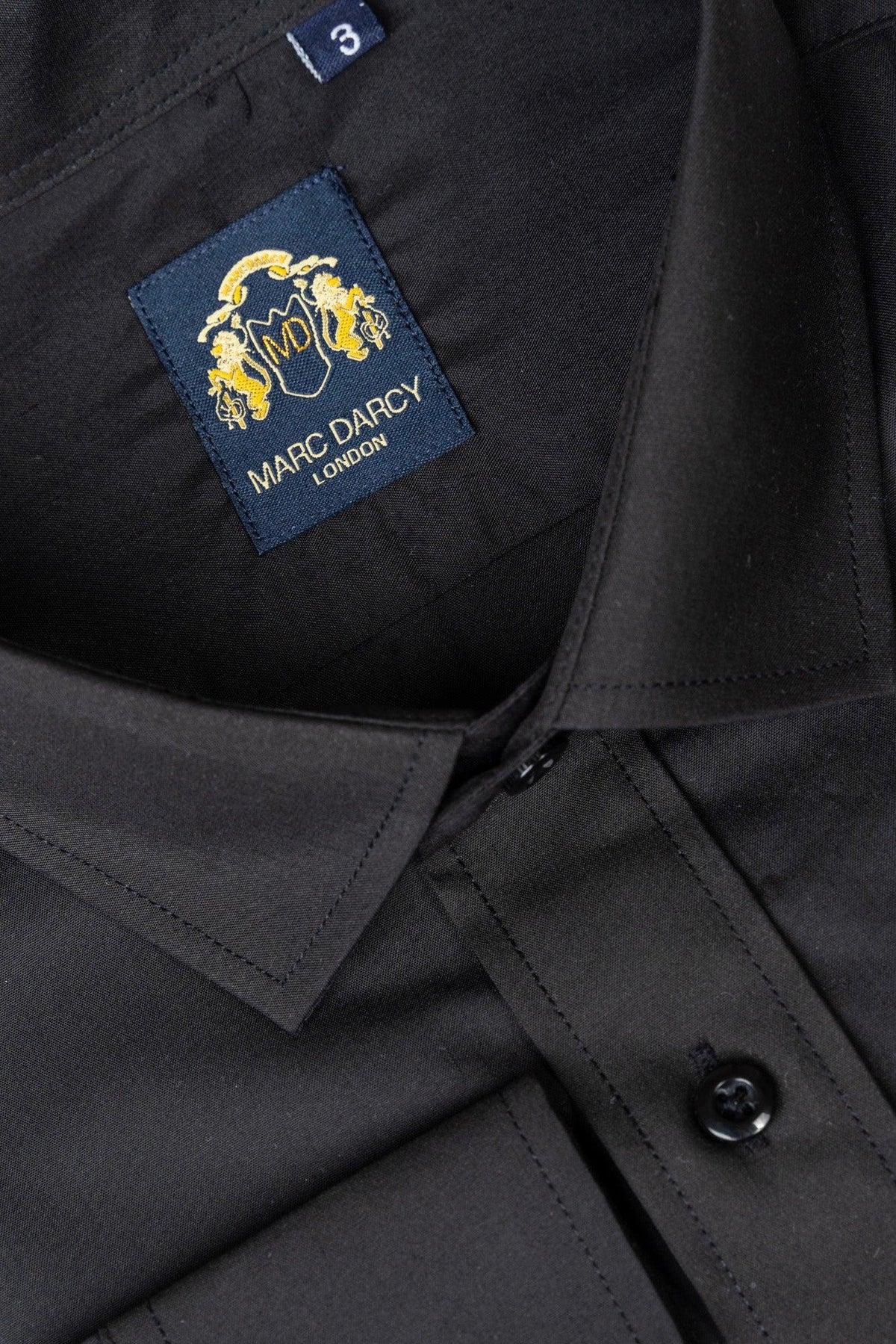 Close-up of the CARTER - Black Long Sleeve Shirt by Marc Darcy, showing the collar, buttons, and inside neckline with a navy and gold brand label plus a visible “3” size tag.