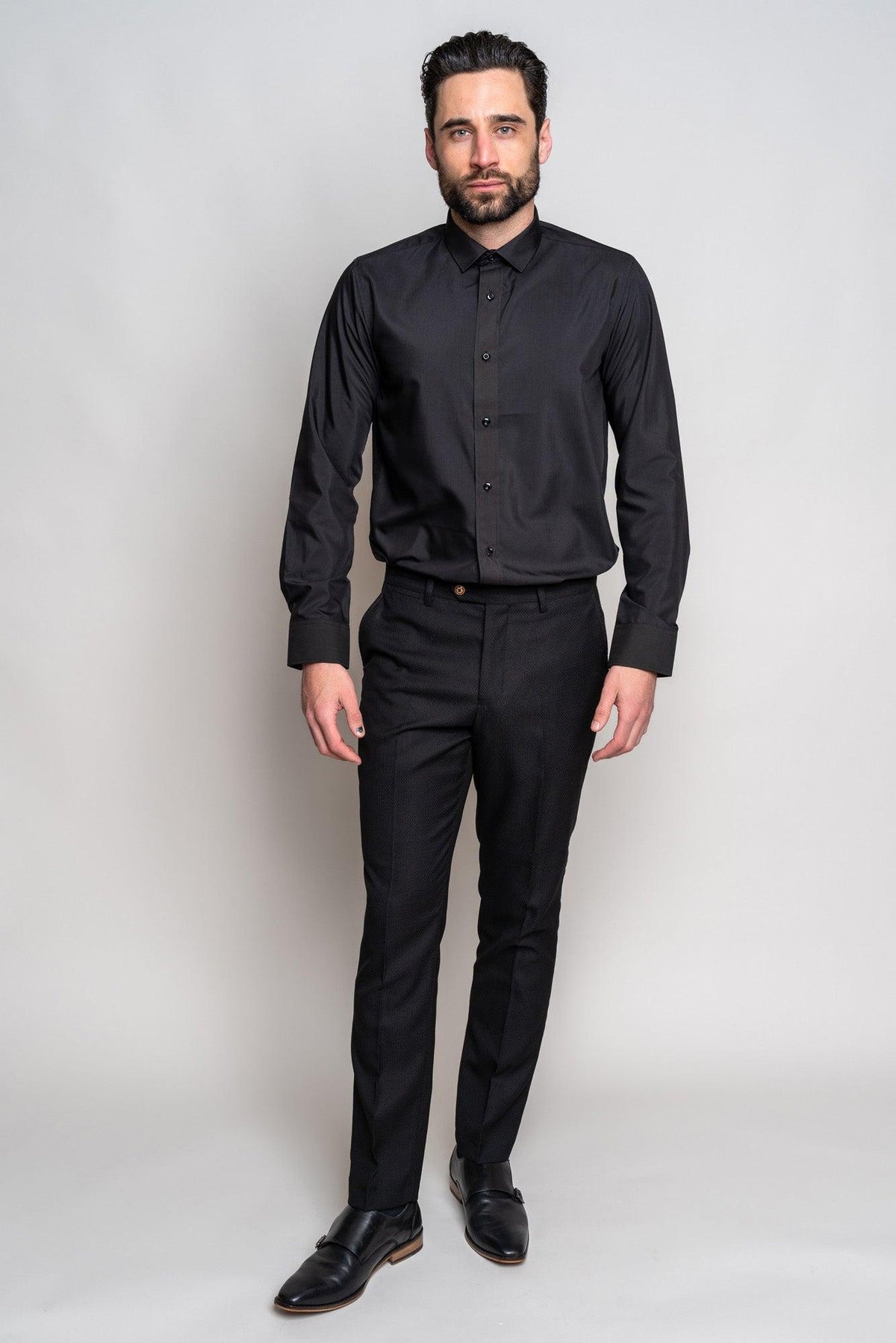 A man with dark hair and a beard stands against a plain light background, wearing the Marc Darcy CARTER black long sleeve shirt, paired with black dress pants and black dress shoes.