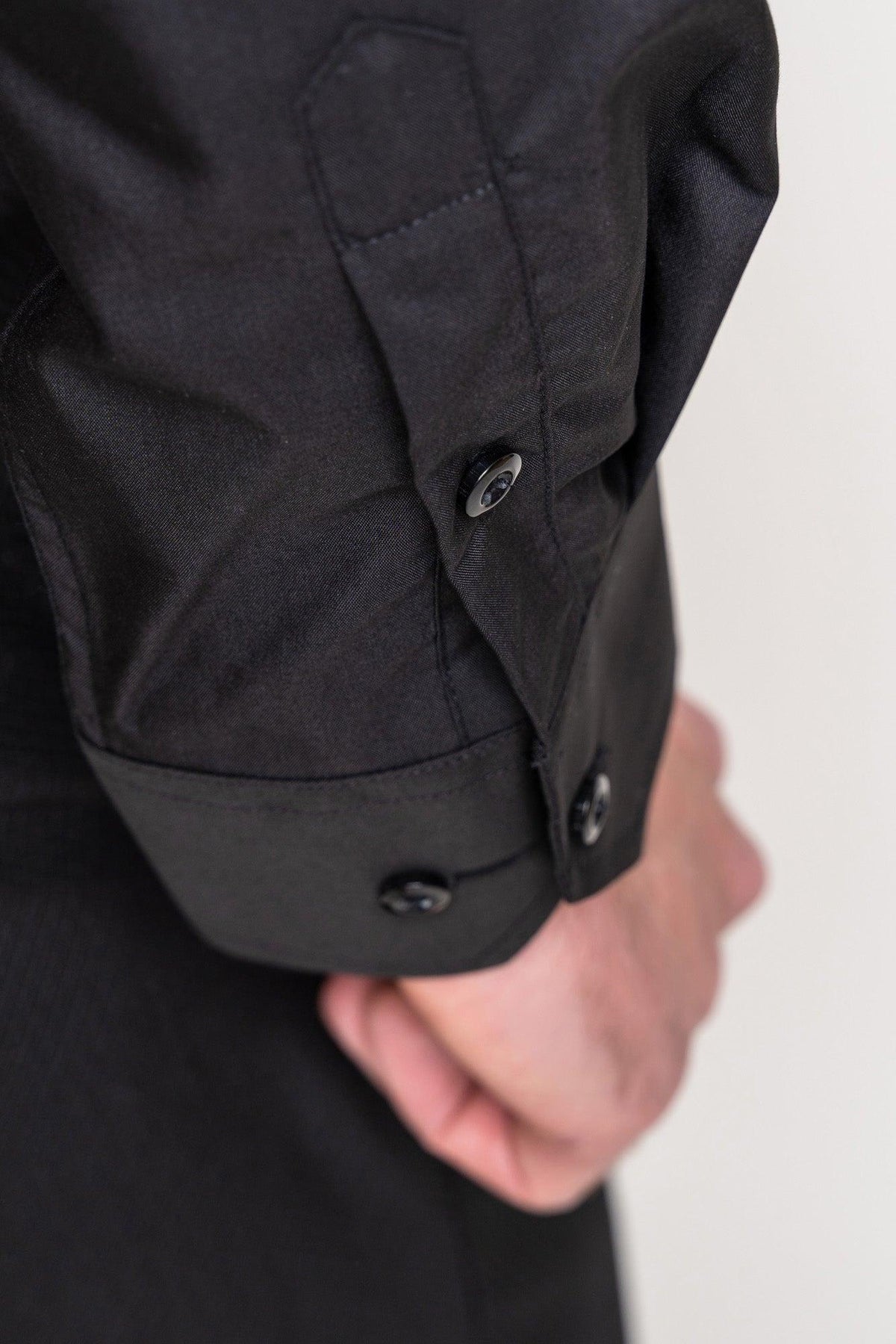 A close-up of a persons arm in the Marc Darcy CARTER - Black Long Sleeve Shirt, highlighting the buttoned cuffs, sleeve detail, part of the hand, classic fit, and spread collar.