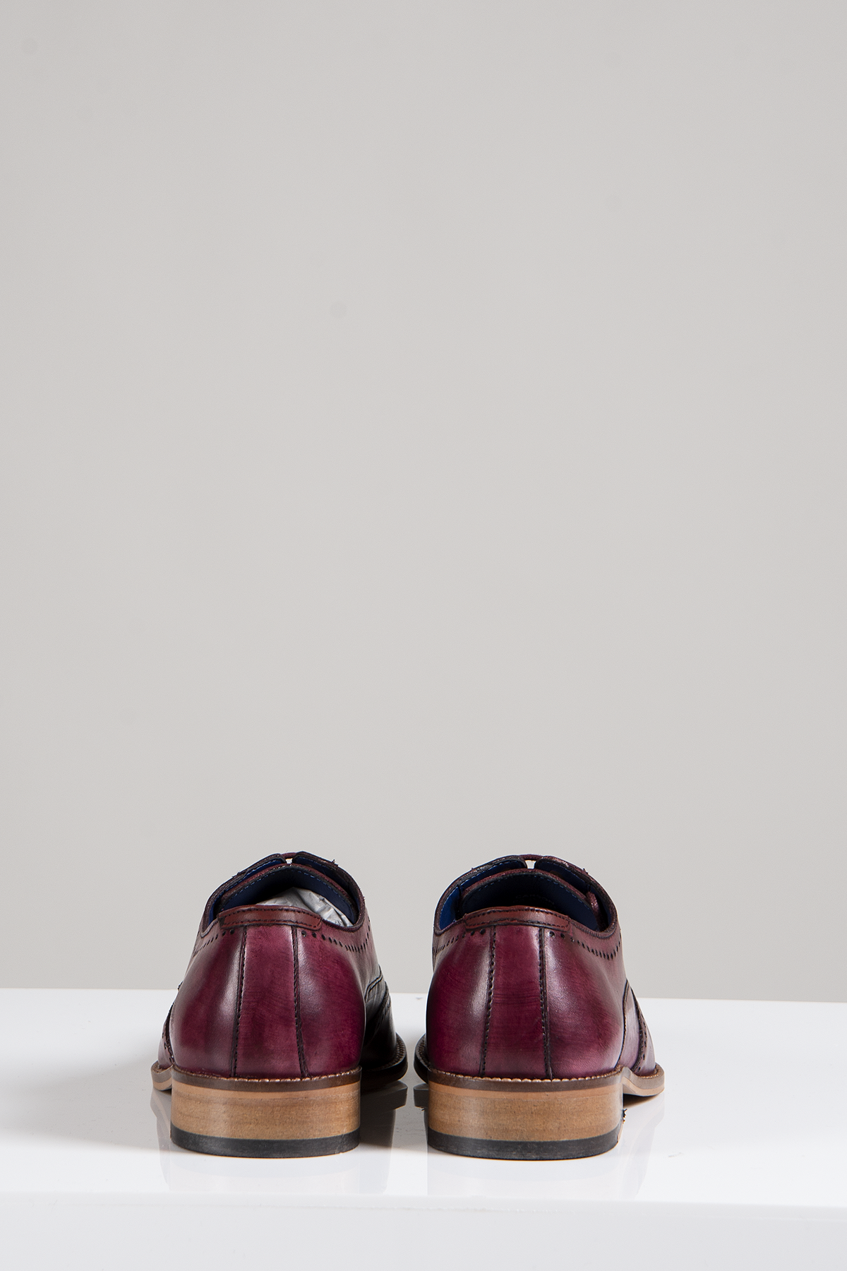 The CARSON - Bordeaux Burgundy Wingtip Oxford Brogue Shoes by Marc Darcy, crafted in full grain leather with light brown soles and hand-stitched detailing, are displayed from the back on a white surface against a light gray background.
