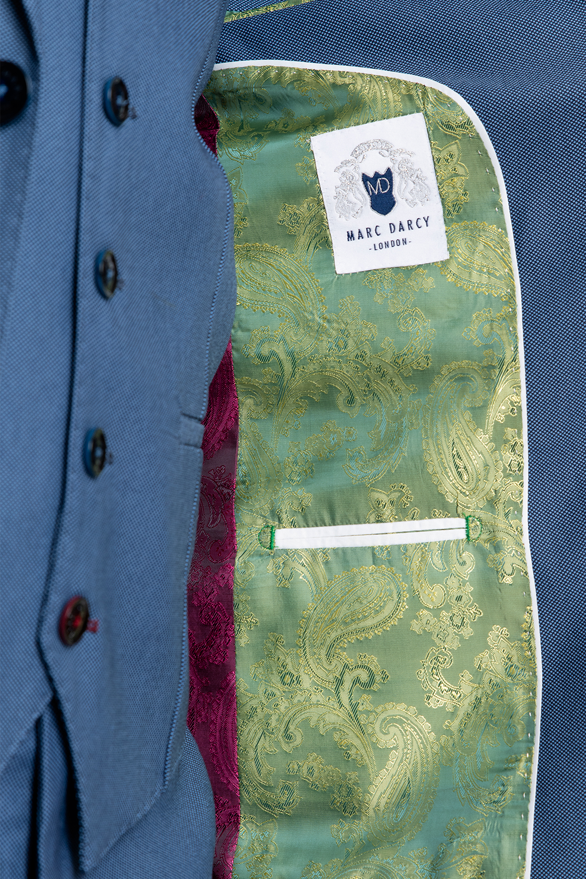 The inside of the DANNY - Sky Tailored Blazer by Marc Darcy features a green and gold paisley lining, maroon inner section, white-trimmed functional pocket, and a Marc Darcy label sewn onto the lining.