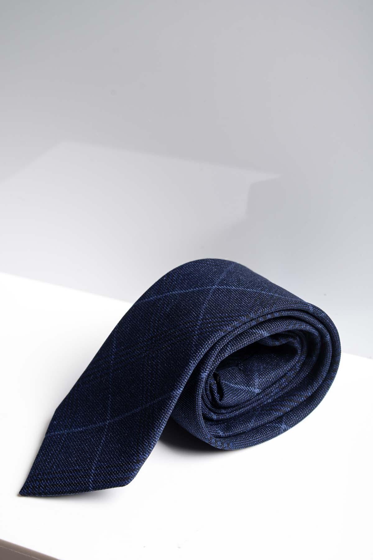 The EDINSON - Navy Sky Check Tie by Accessory, featuring a subtle plaid pattern, is elegantly rolled on a white surface and highlights the timeless style of a handmade design.