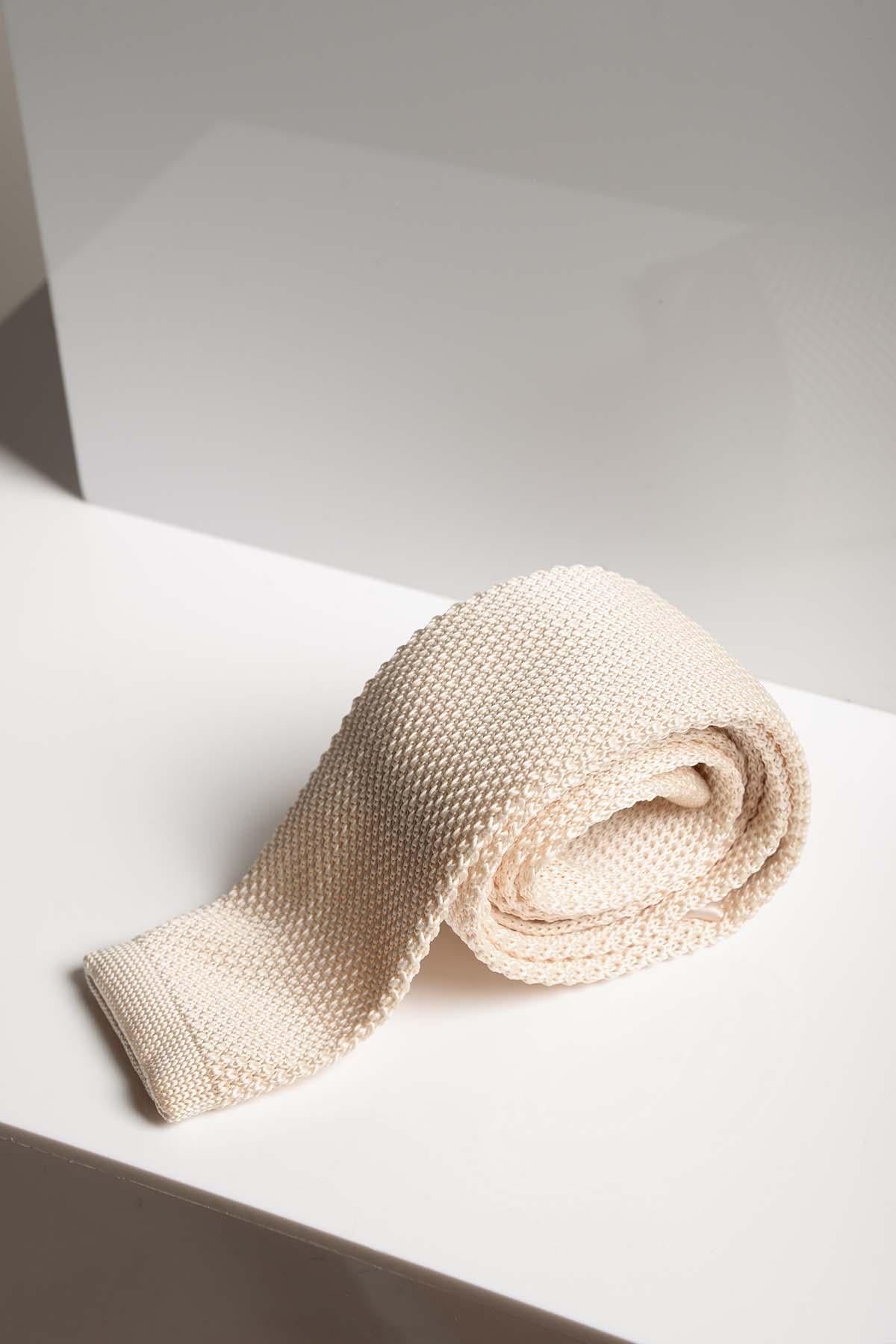 The KT - Cream Knitted Tie by Accessory is loosely rolled and displayed on a white surface with soft lighting, highlighting its elegance—making it a perfect wedding accessory for any formal occasion.