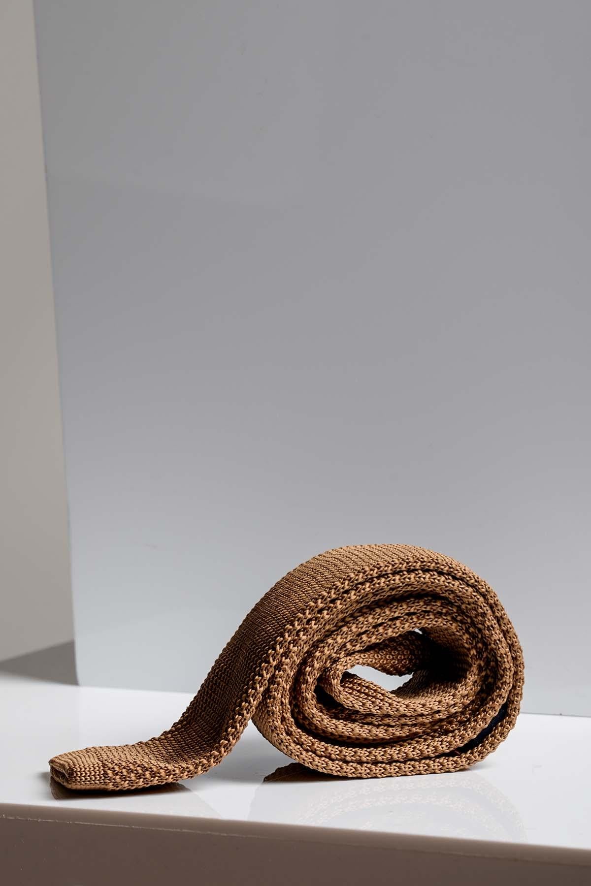 The Accessory KT - Dark Oak Knitted Tie is shown rolled up on a white surface against a gray background, offering an elegant choice for wedding attire.