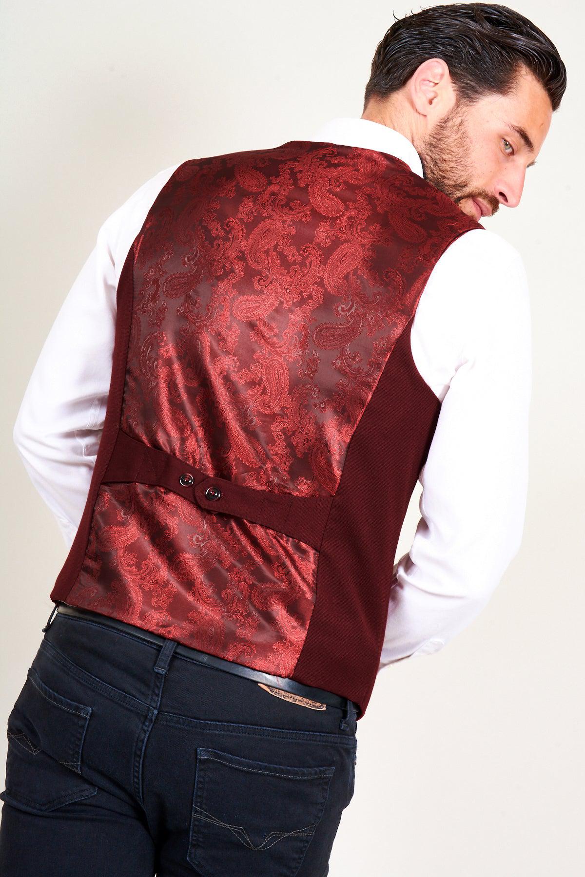 A man wearing the marcdarcy KELLY - Wine Single Breasted Waistcoat with a shiny, paisley-patterned back panel and a white shirt, viewed from behind and slightly to the side, paired with dark jeans.