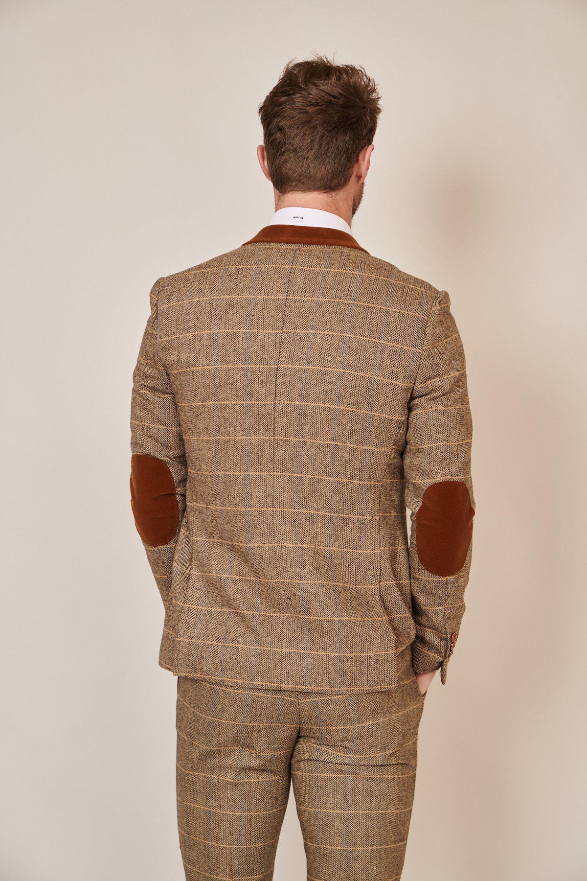 A man in the marcdarcy Blogger Style | DX7 Suit As Worn By Jonny Hammond, with brown elbow patches, stands facing away from the camera against a plain light background, showcasing its stylish craftsmanship and slim fit.