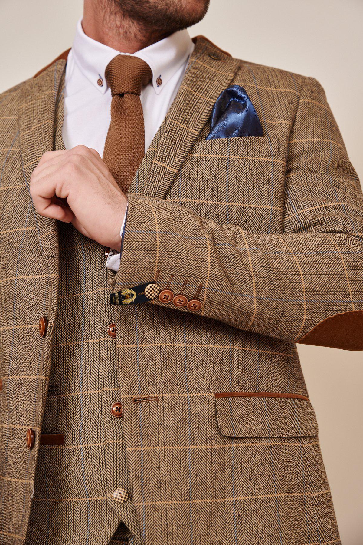 A man wearing the marcdarcy Blogger Style | DX7 Suit As Worn By Jonny Hammond with a matching vest, white shirt, brown tie, and blue pocket square adjusts his jacket. His face is partially out of frame.