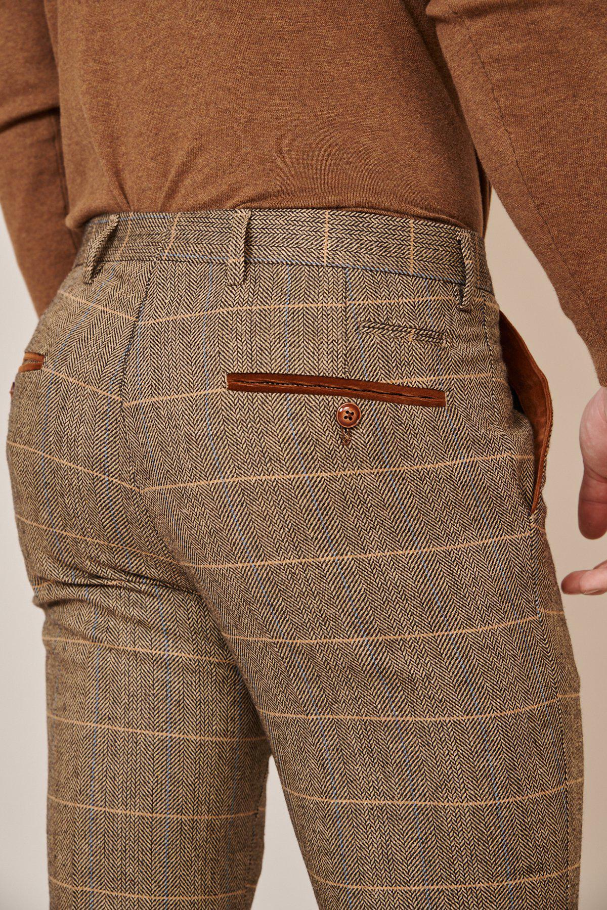 A close-up of a person wearing the marcdarcy Blogger Style | DX7 Suit As Worn By Jonny Hammond, brown plaid trousers and a brown top, highlighting the back pockets with brown trim and a button on one pocket.