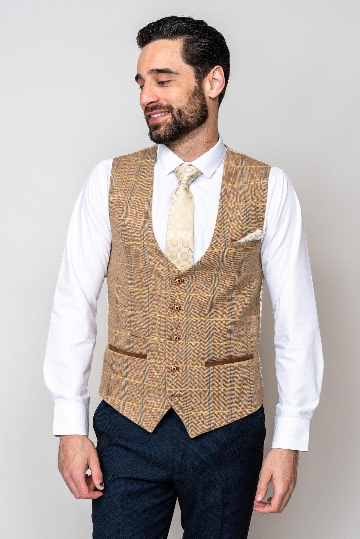 A man in a white shirt, marcdarcy DX7 - Oak Tweed Check Waistcoat, and navy pants smiles while looking down to the left, capturing a classic heritage style.