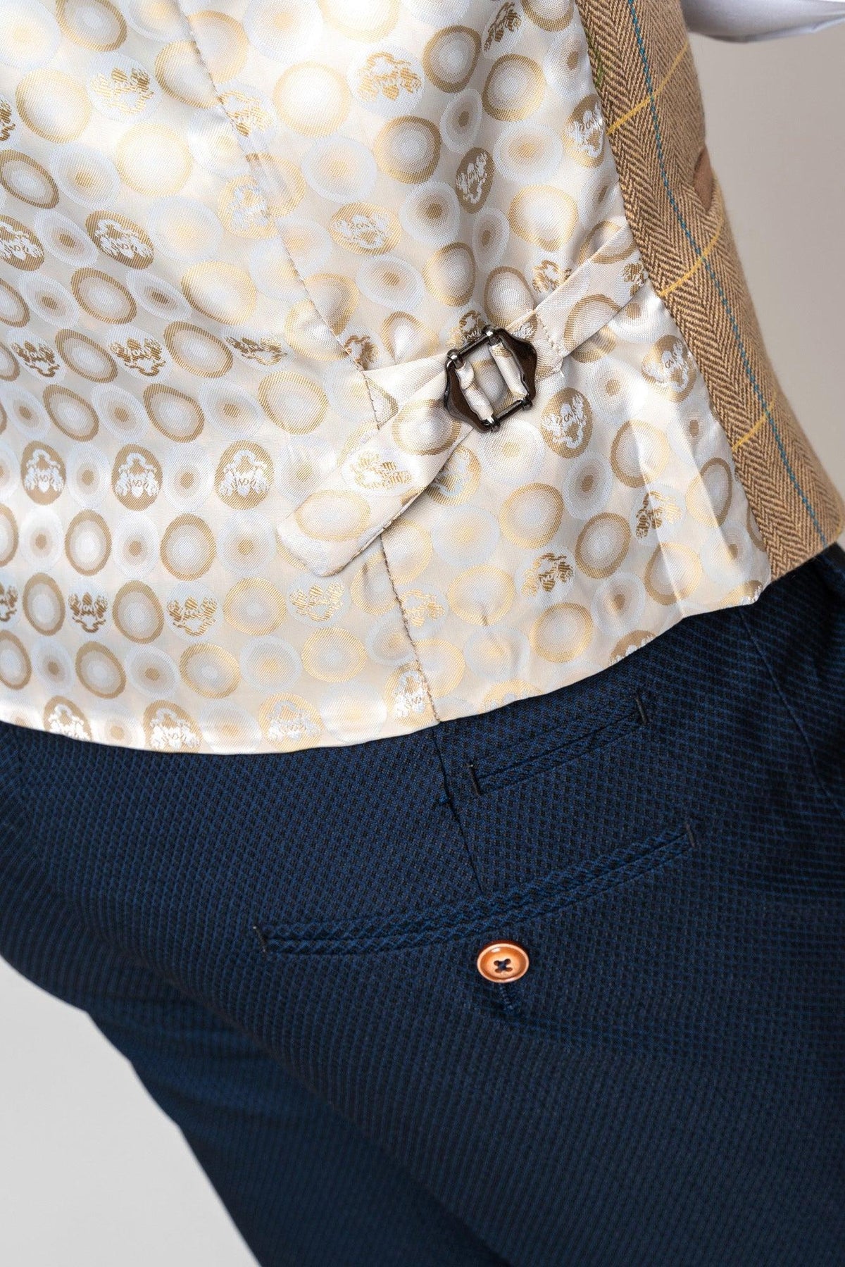 A close-up of the marcdarcy DX7 - Oak Tweed Check Waistcoat’s vest lining with a gold and white circular pattern, paired with dark blue herringbone slim fit pants and an orange button.