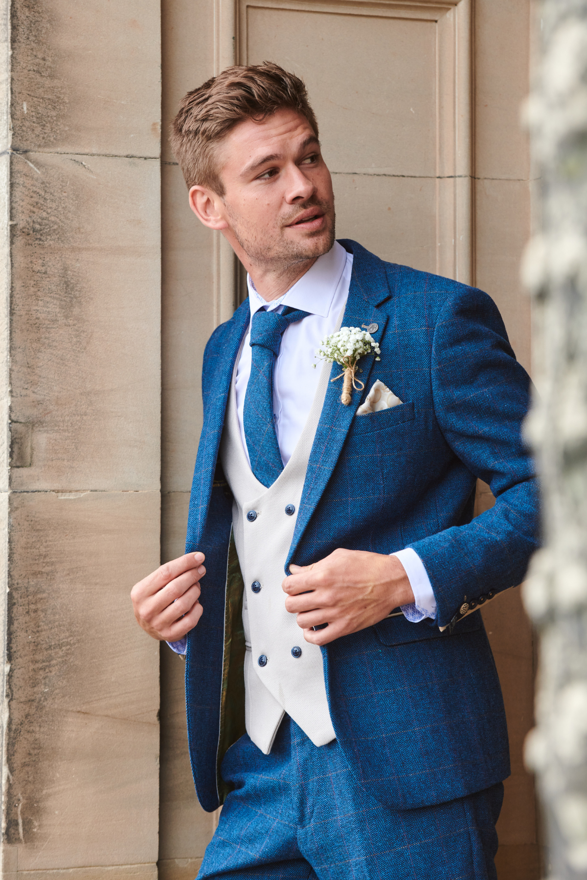 A man in the marcdarcy DION Blue Tweed Check Suit with Kelvin Stone Waistcoat—an elegant groom suit complete with matching tie, pocket square, and boutonnière.