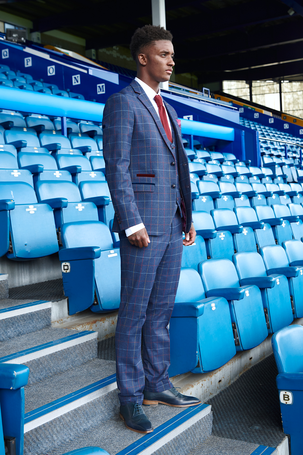 Demarai Gray stands on stadium stairs wearing the marcdarcy Drake Navy Suit from The Everton Collection.