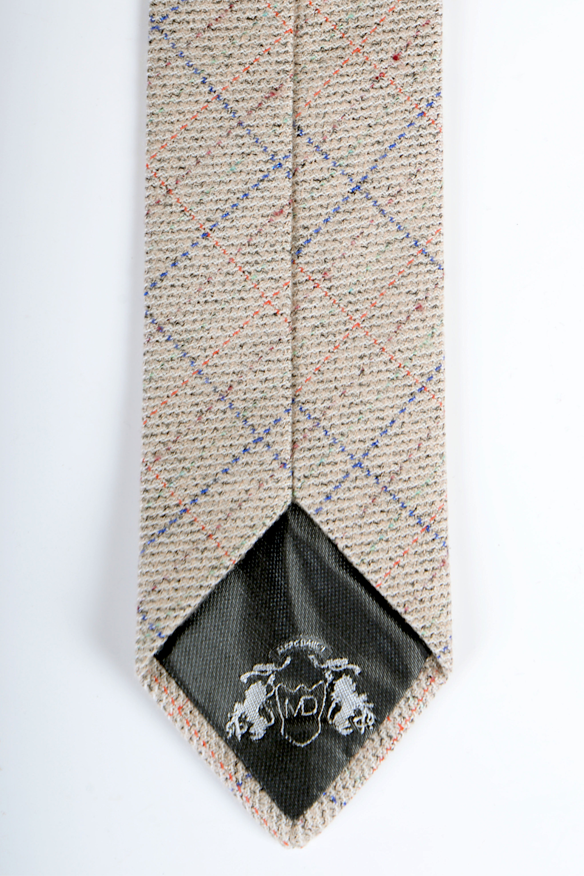 The Harding - Cream Tweed Check Tie by Accessory features a beige wool tweed with blue, red, and yellow plaid. Its tip has a black lining with a white embroidered crest of two lions and the initials MD. A versatile cream neutral tie.