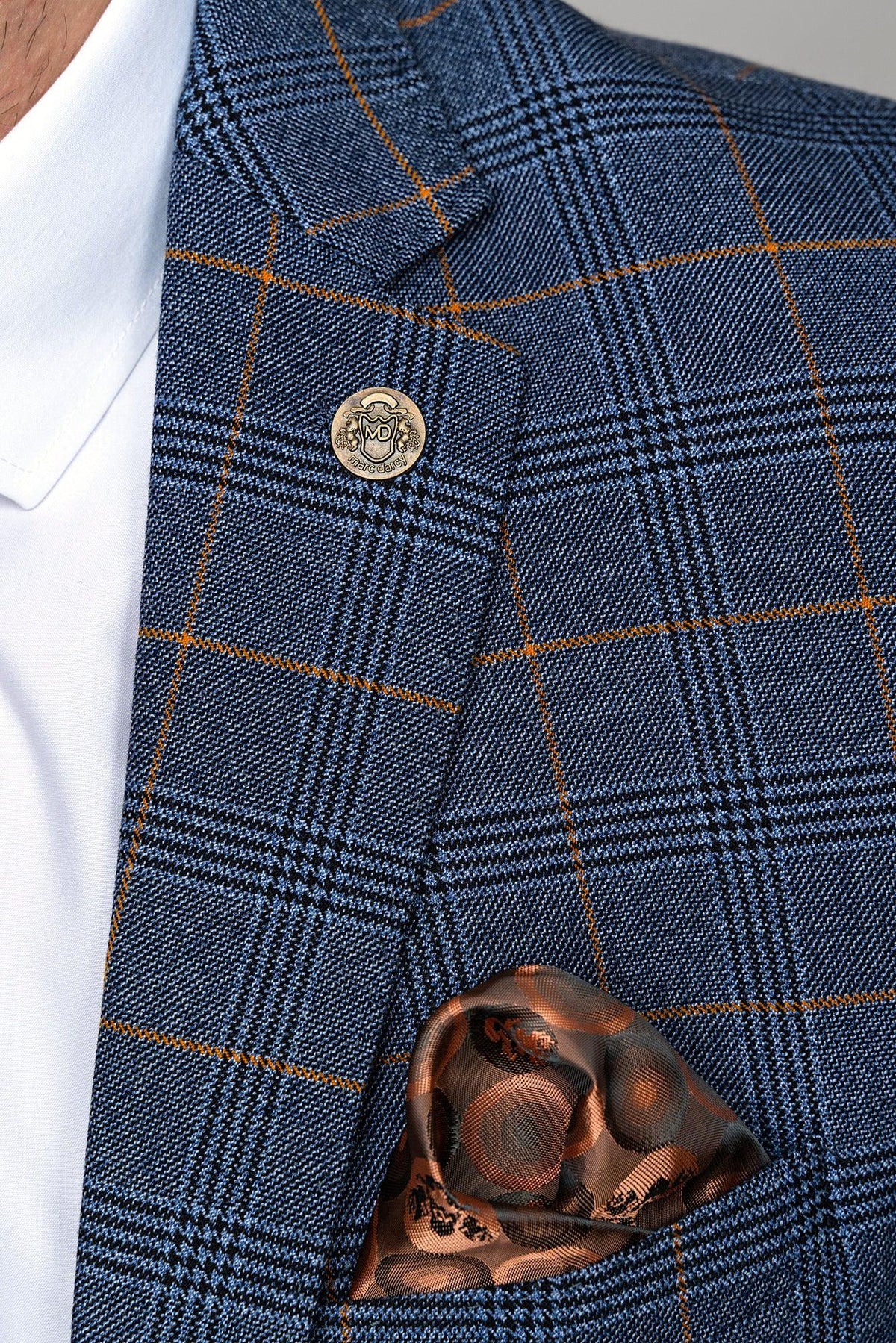 A close-up of a person wearing the marcdarcy JENSON Sky Blue Check Suit with Kelvin Tan Waistcoat, paired with a white shirt, metallic lapel pin, and patterned brown silk pocket square.