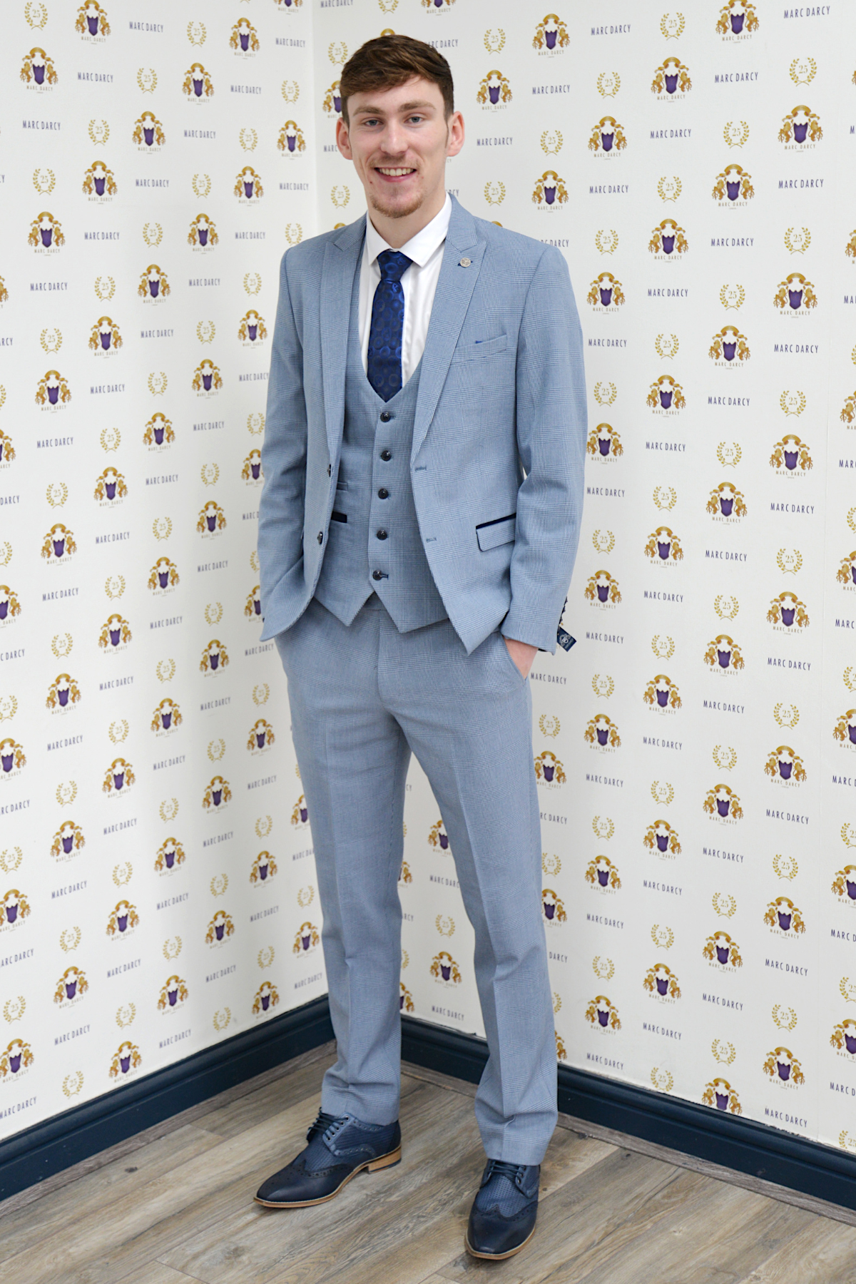 Everton midfielder James Garner wears the marcdarcy Bromley Sky Three Piece Suit, posing with hands in pockets and smiling in front of a marcdarcy branded backdrop on a wooden floor.