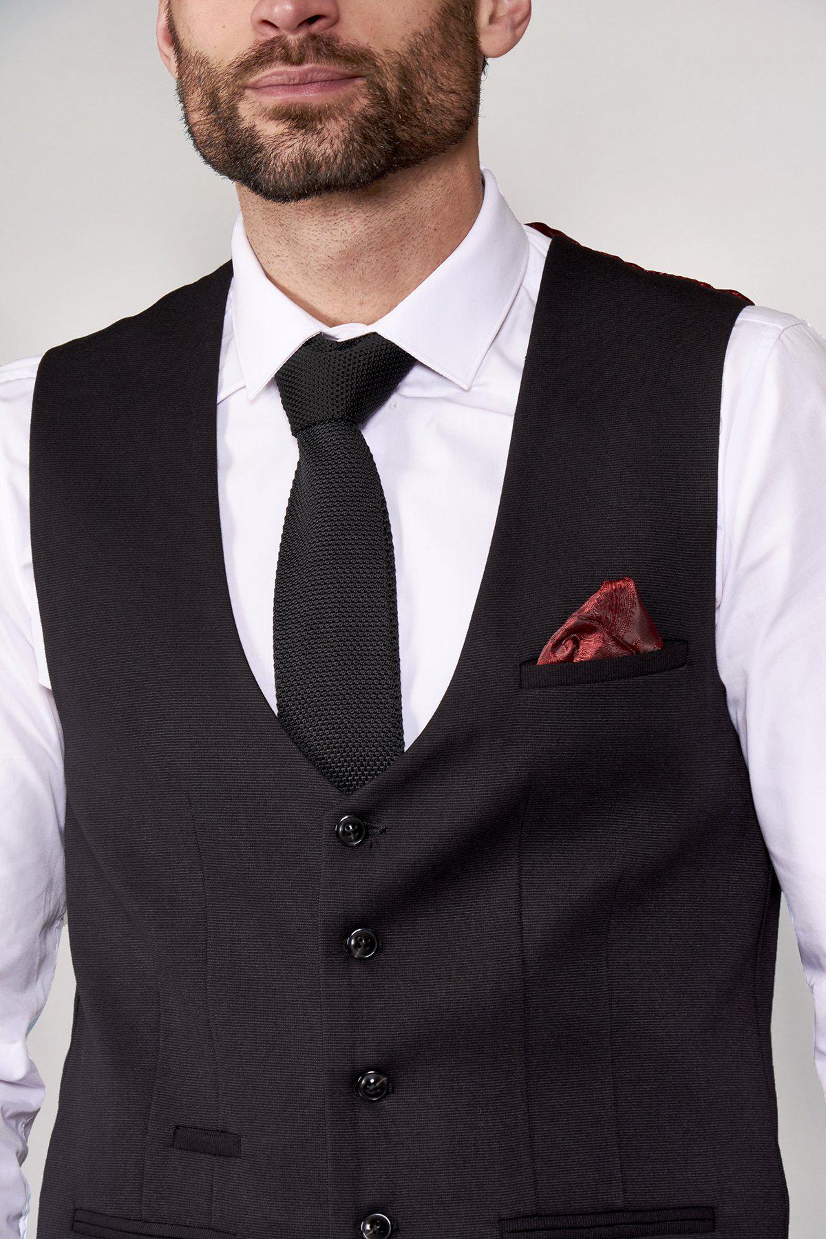 A bearded man wears a slim fit white dress shirt, black textured tie, and the marcdarcy KELLY Black Single Breasted Waistcoat with buttons. A red pocket square adds contrast. The image is cropped at the shoulders.
