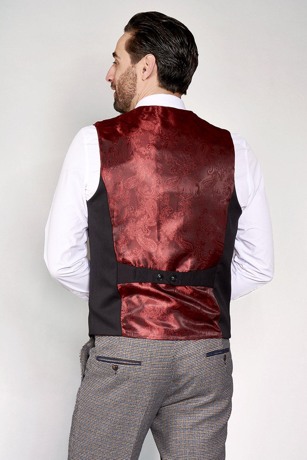 A man in a slim fit white dress shirt, gray checkered trousers, and the marcdarcy KELLY black single breasted waistcoat stands facing away from the camera, showcasing the back details of his formalwear.