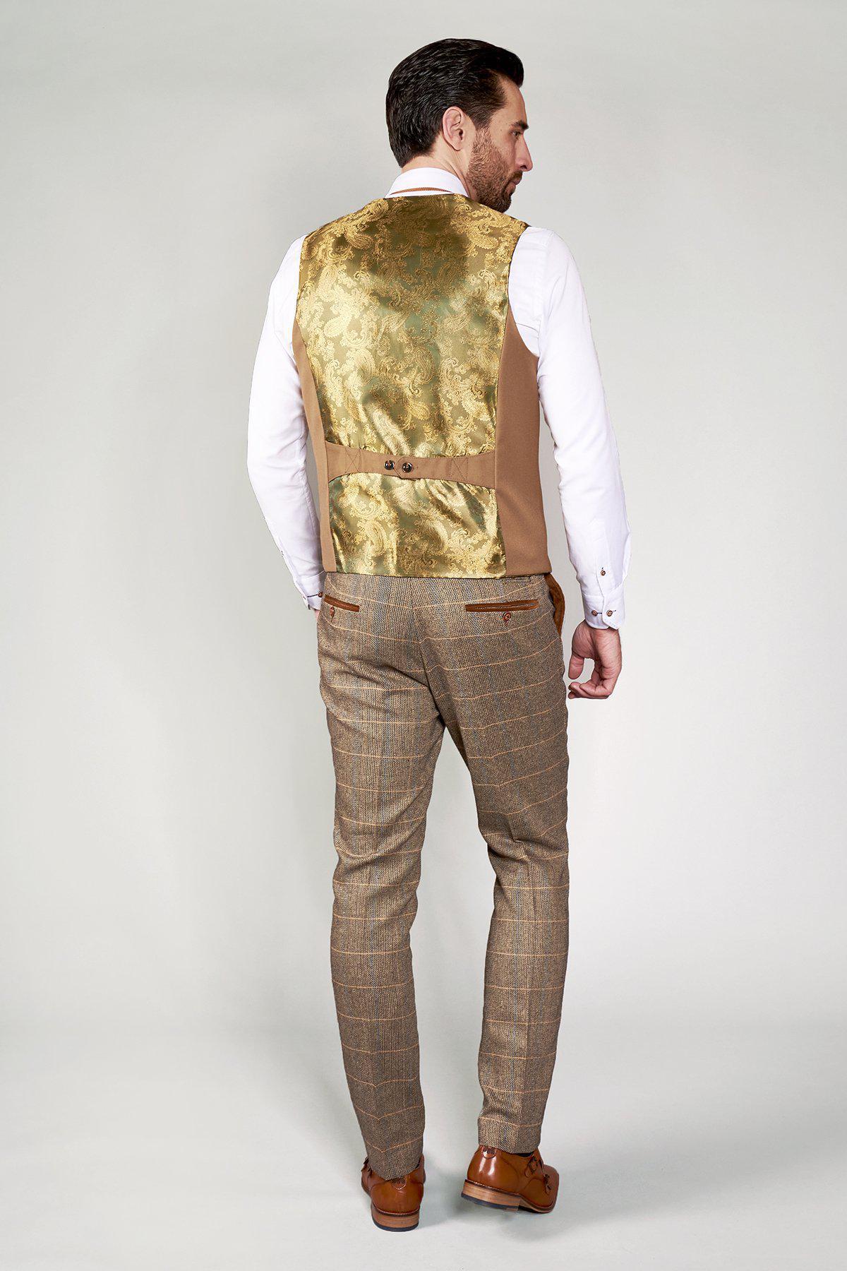 A man with dark hair, wearing a white shirt, slim fit brown checked trousers, and the marcdarcy KELLY Tan Double Breasted Waistcoat with gold brocade back, stands against a plain light background in classic British style.