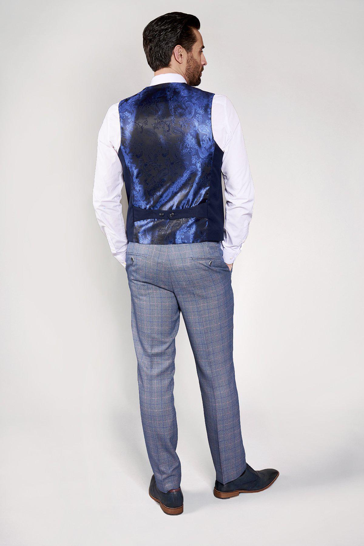 A man faces away from the camera, wearing a marcdarcy slim fit white shirt, KELLY blue double breasted waistcoat, gray plaid trousers, and dark shoes against a light plain background for a formal look.