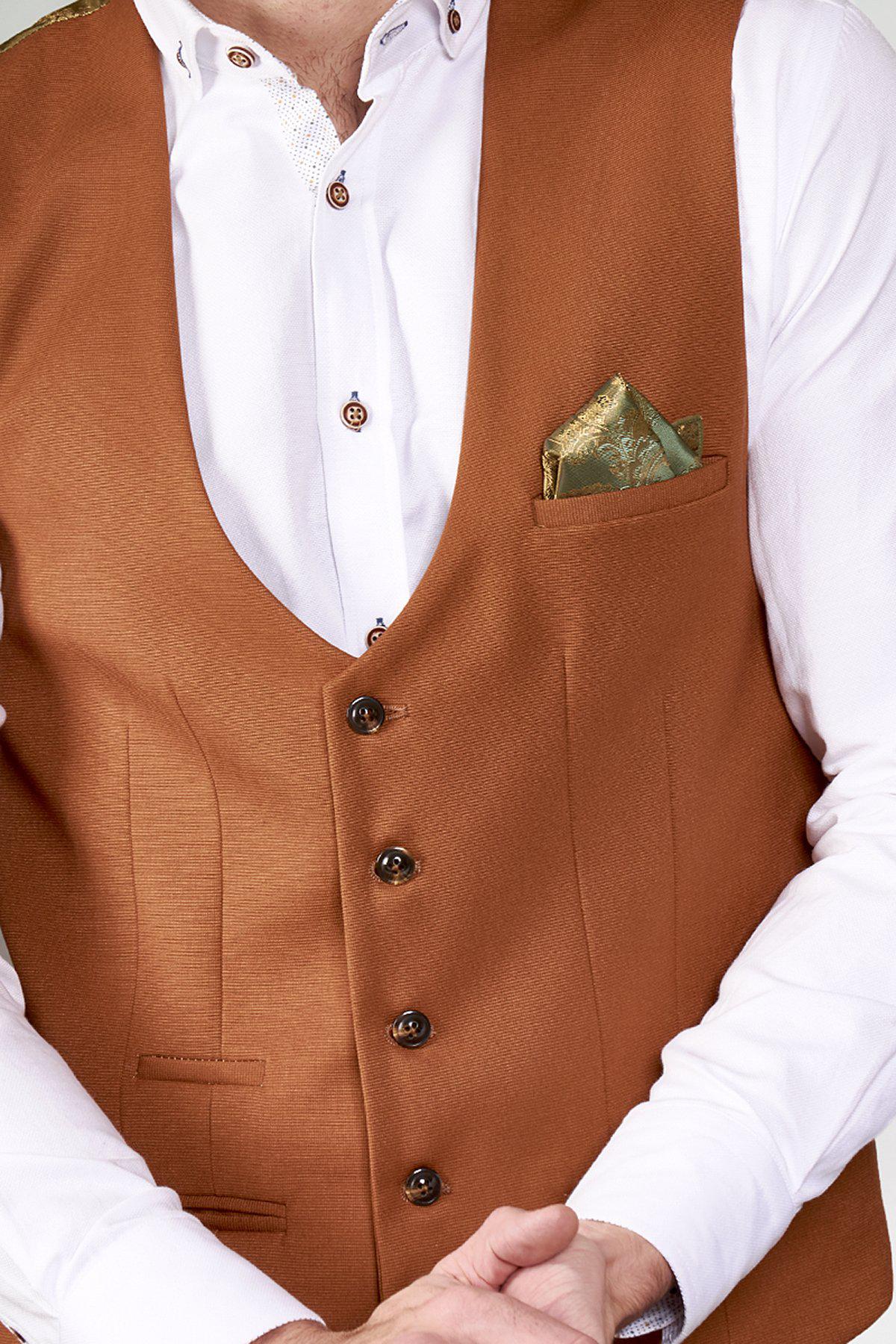 A person wears a white dress shirt with brown buttons and the marcdarcy KELLY - Dark Tan Single Breasted Waistcoat. A green and gold patterned pocket square highlights the gold paisley lining. Their hands are clasped in front.
