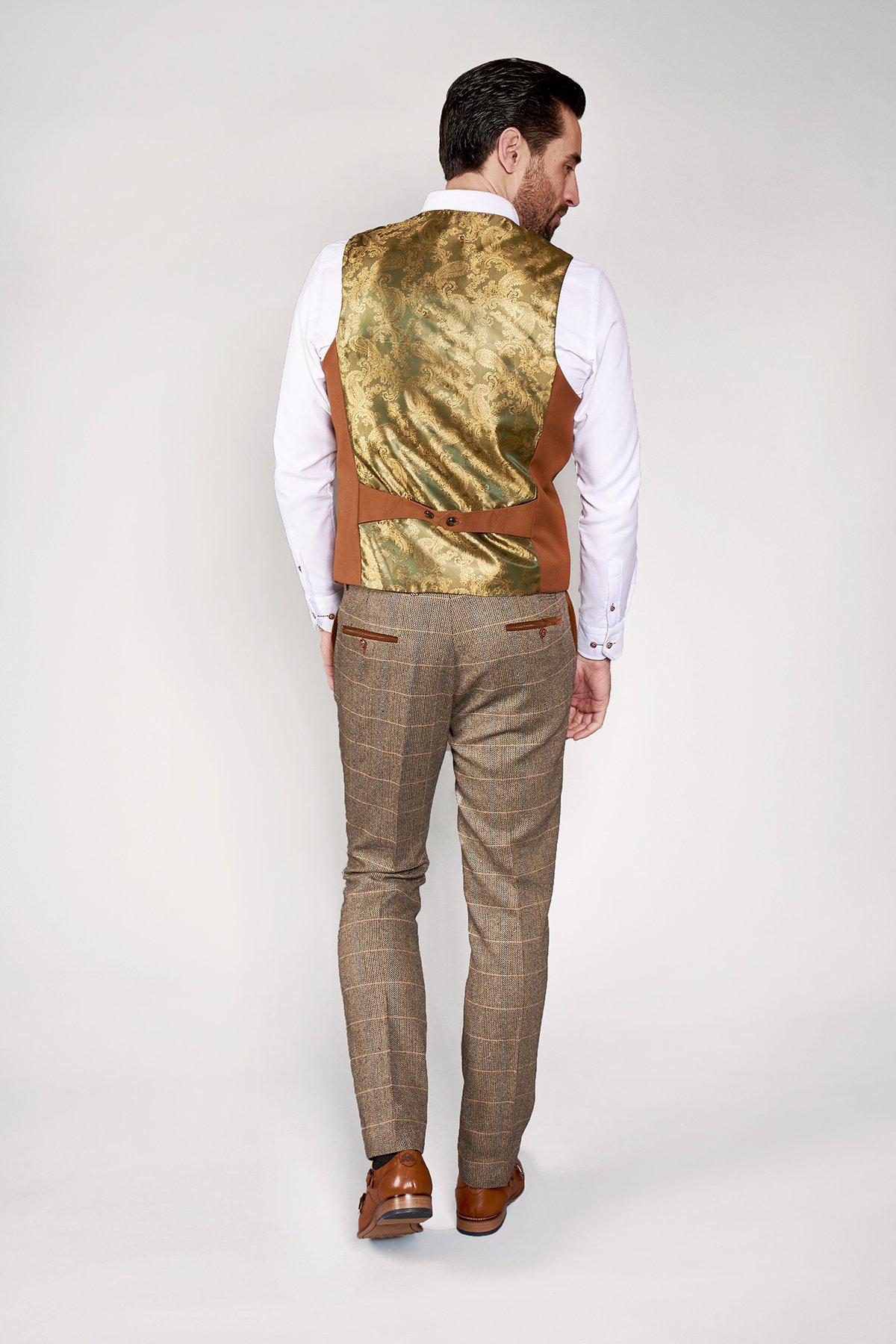 A man faces away, wearing the marcdarcy KELLY Dark Tan Single Breasted Waistcoat with gold paisley lining, paired with a white shirt, brown plaid trousers, and brown dress shoes against a plain light background.
