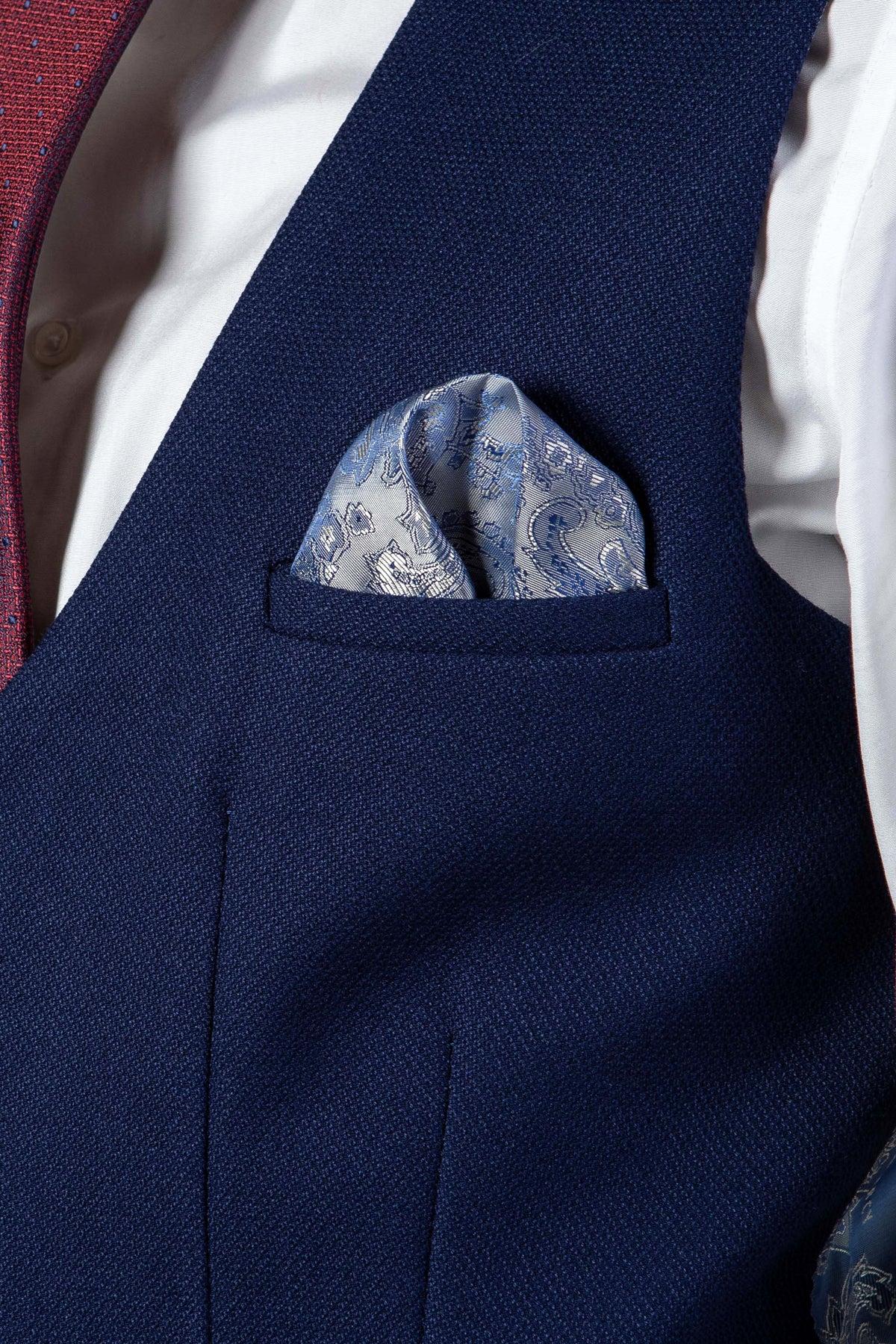 A close-up of someone wearing the marcdarcy KELVIN Royal Blue Single Breasted Waistcoat over a white dress shirt and red tie, with a light blue paisley pocket square neatly folded in the chest pocket.