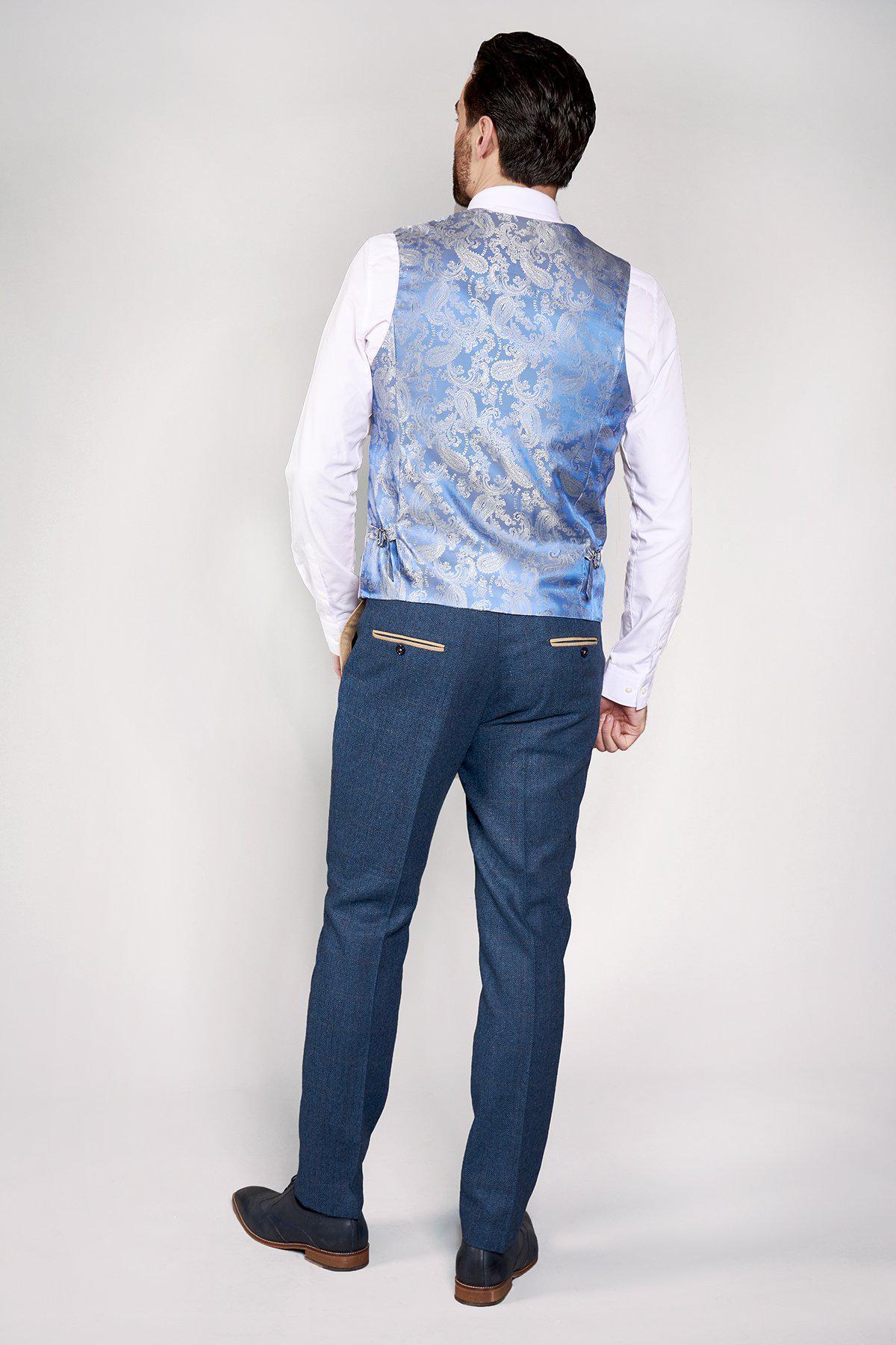 A man faces away wearing the marcdarcy DION Blue Tweed Check Suit with Kelvin Stone Waistcoat, styled with a white shirt and dark shoes—a sophisticated modern groom look against a plain background.
