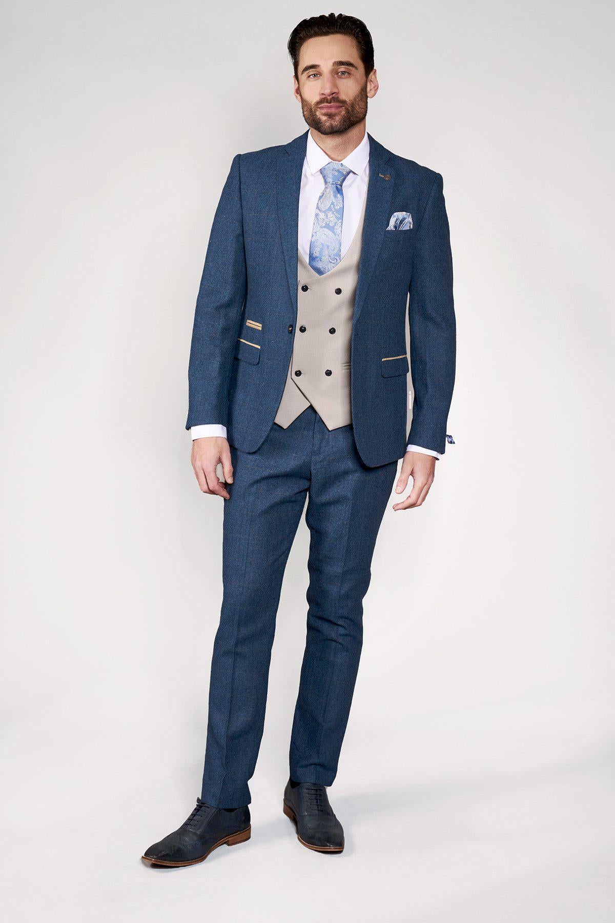 A man stands against a plain background wearing the marcdarcy DION Blue Tweed Check Suit with Kelvin Stone Waistcoat, white shirt, patterned blue tie, pocket square, and dark dress shoes—the perfect groom suit.