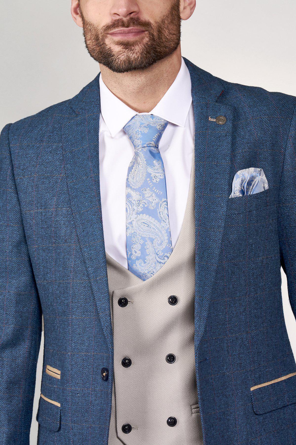 A man models the marcdarcy DION Blue Tweed Check Suit with Kelvin Stone Waistcoat, white shirt, and pale blue paisley tie with matching pocket square—an elegant groom attire. The image is cropped above the nose.
