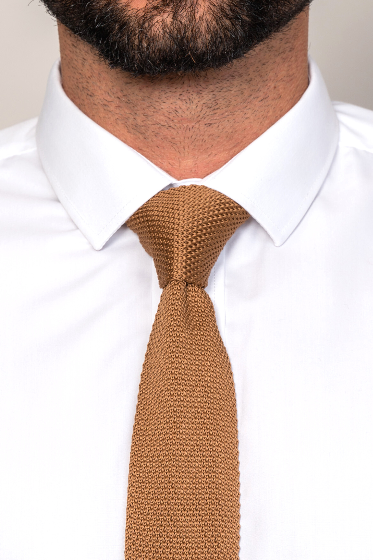 A close-up of a man in a white dress shirt and the Accessory KT - Dark Oak Knitted Tie, an ideal wedding accessory, with a neatly trimmed beard visible at the top of the image.