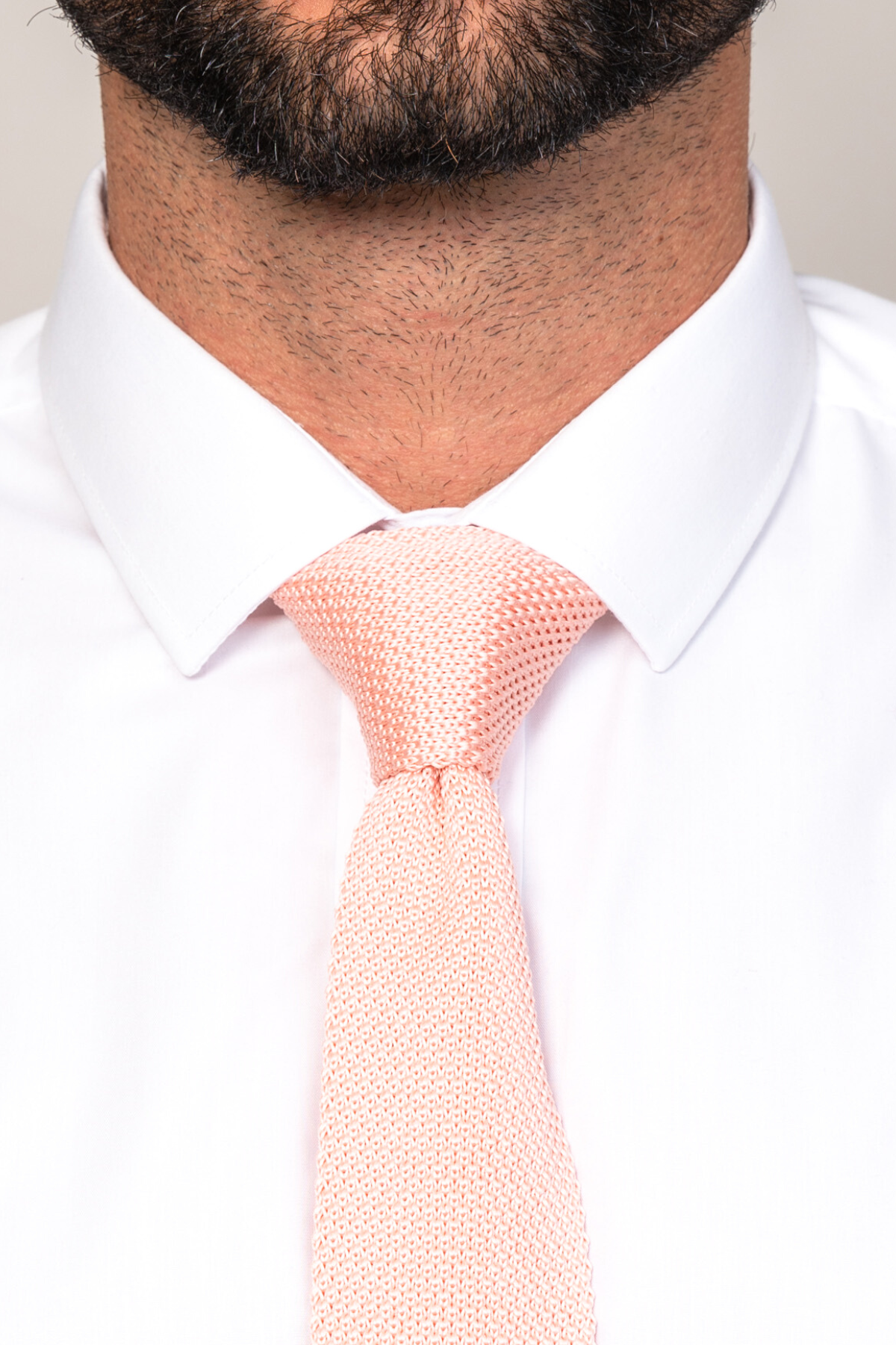 Close-up of a man wearing Accessory’s KT - Peach Knitted Tie and a white dress shirt. Only his trimmed beard, lower face, neck, and upper chest are visible—a perfect spring-summer or wedding accessory.