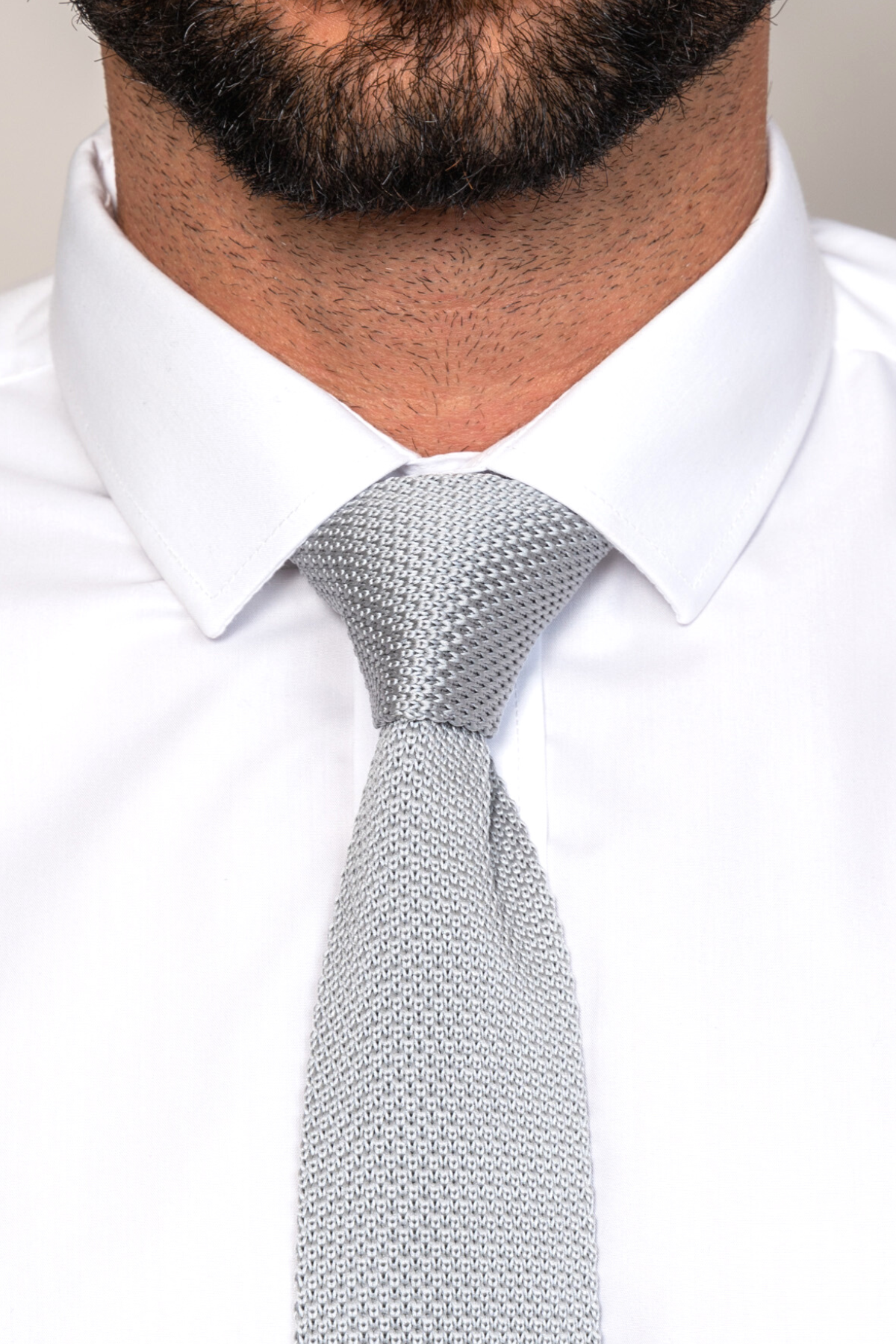 A close-up shows a person wearing the Accessory KT - Silver Grey Knitted Tie with a modern textured design and a white dress shirt; the lower half of their face and beard are partially visible.