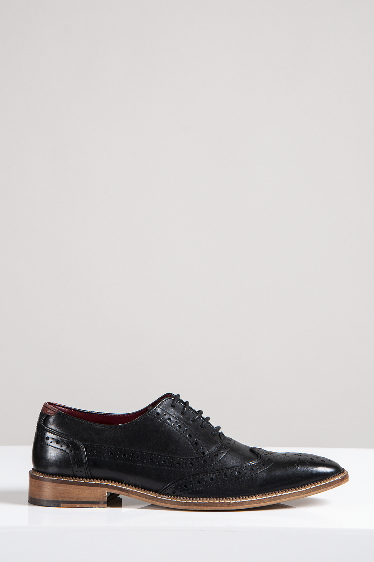 The LARKIN Black Leather Brogue Shoe by Marc Darcy, with decorative perforations, a brown sole, and black laces, is displayed on a white surface against a plain light gray background.