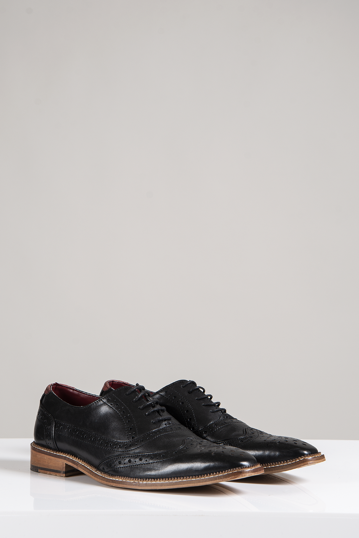 The LARKIN Black Leather Brogue Shoe by Marc Darcy features decorative perforations, brown soles, and dark laces, shown on a white surface with a light gray background.